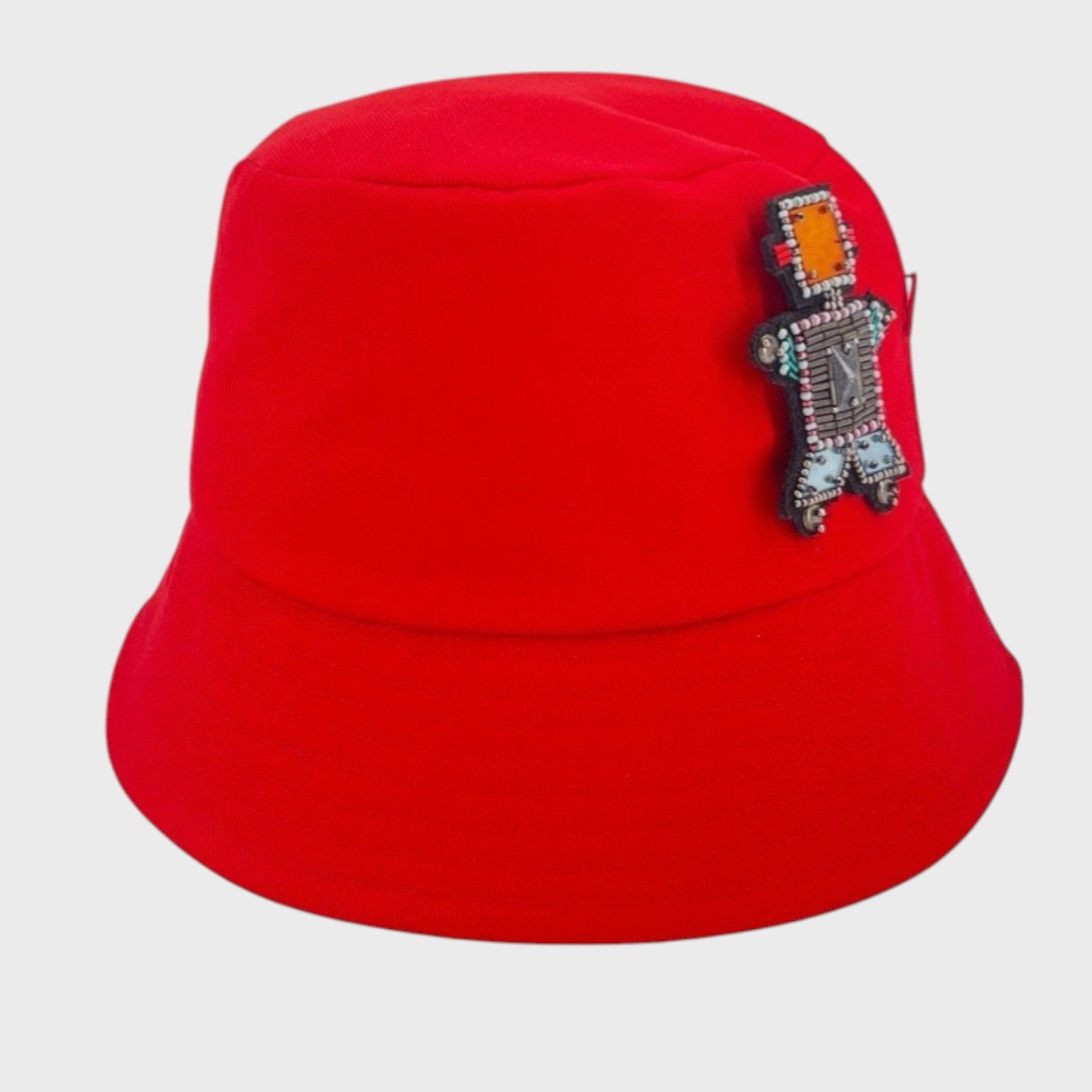 A red cotton bucket hat with a robot with an orange stoned face brooch. 
