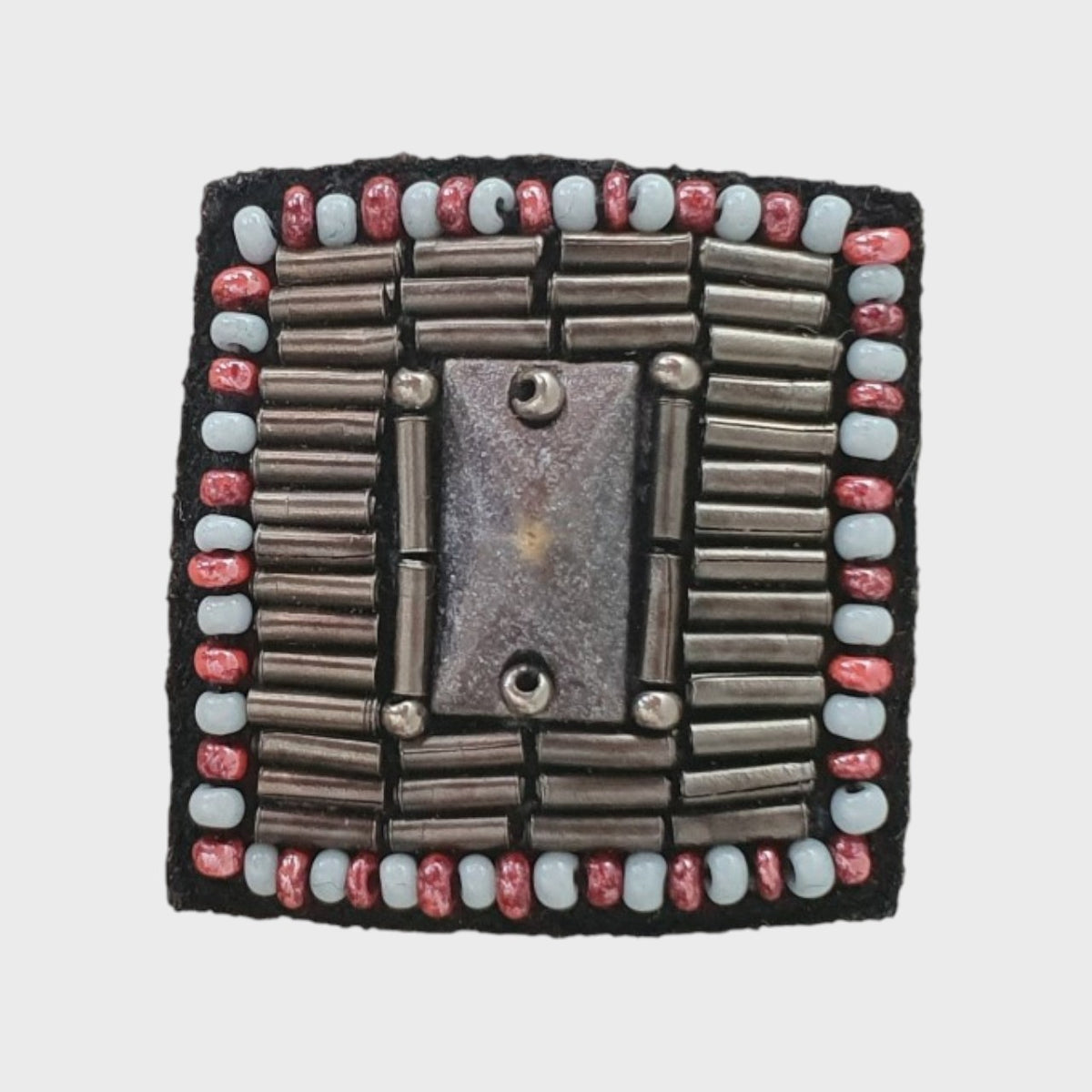 An embroidered brooch representing a button with silver and red details and pearls. 