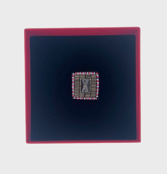 An embroidered brooch representing a button in a red box. 