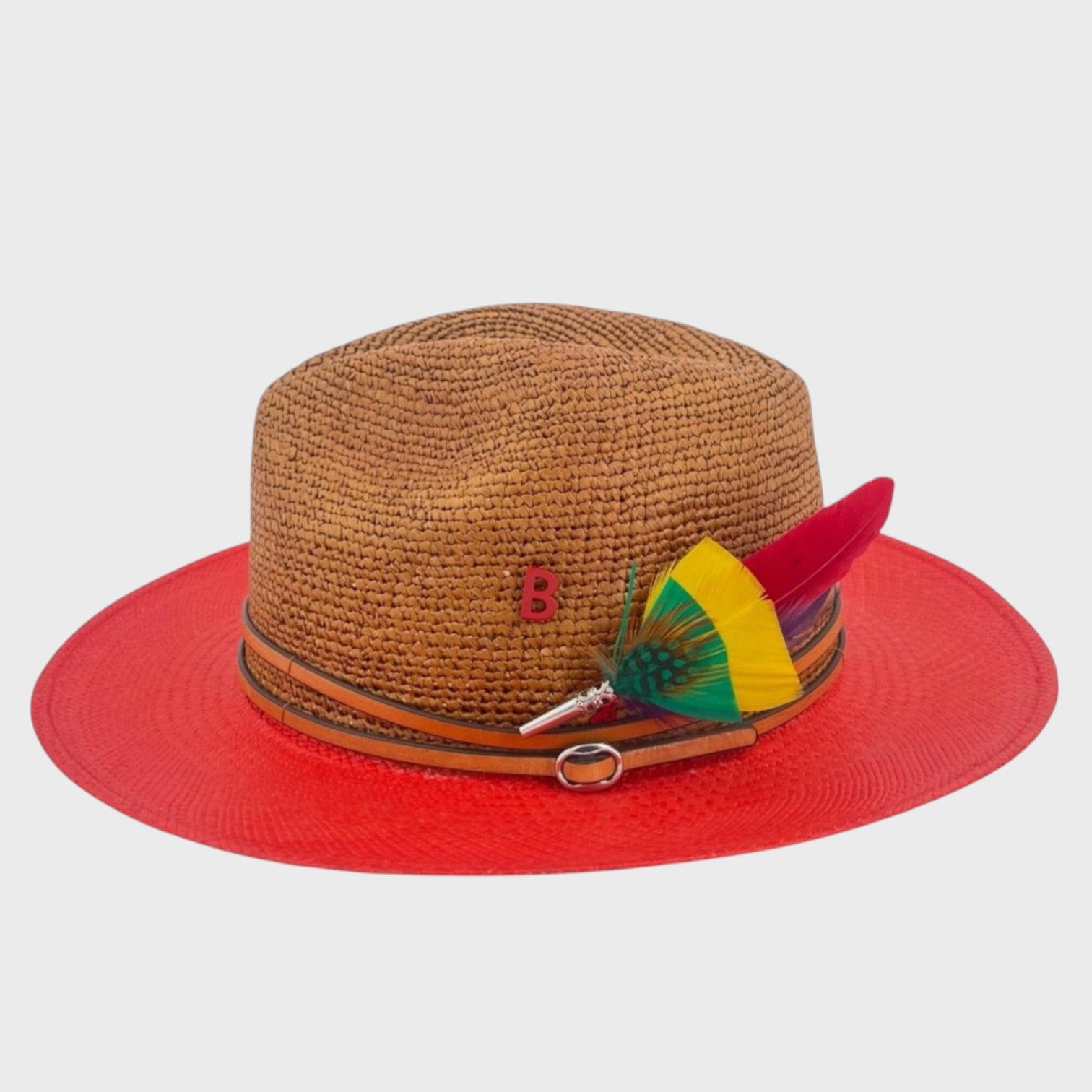A red and brown raffia hat with a brown leather band around it and a yellow, green, red and purple feather brooch pinned on it. 