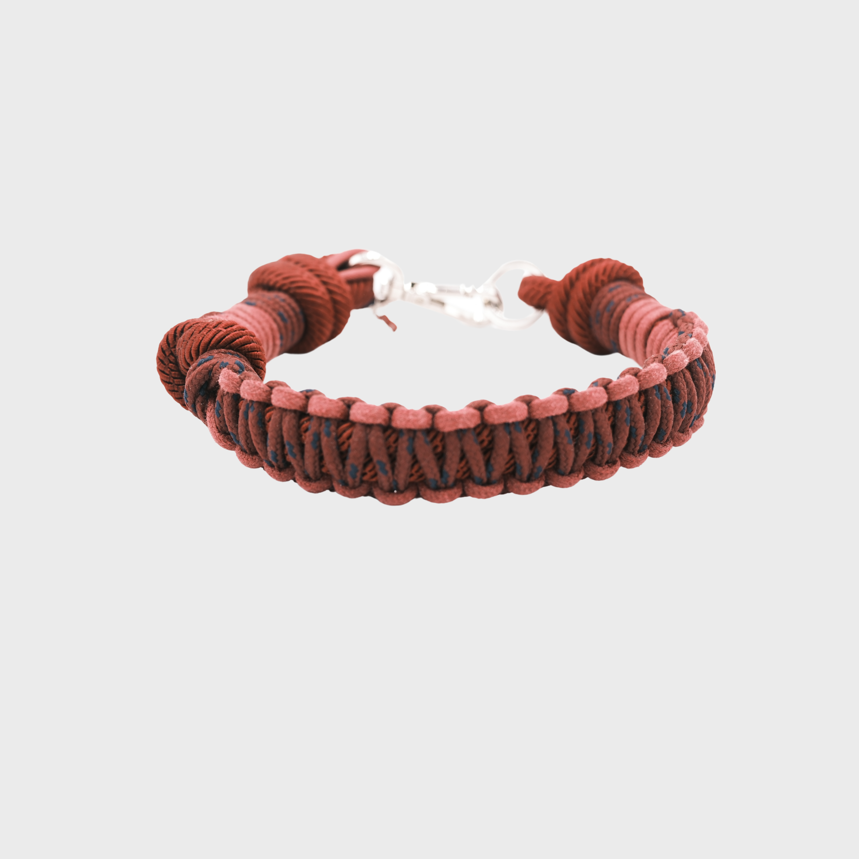 A braided macramé cord collar in shades of red and pink with a silver clasp, centered on a light gray background.