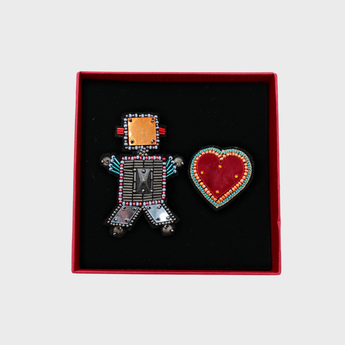 Two embroidered brooches representing a robot and a heart in a red box. 