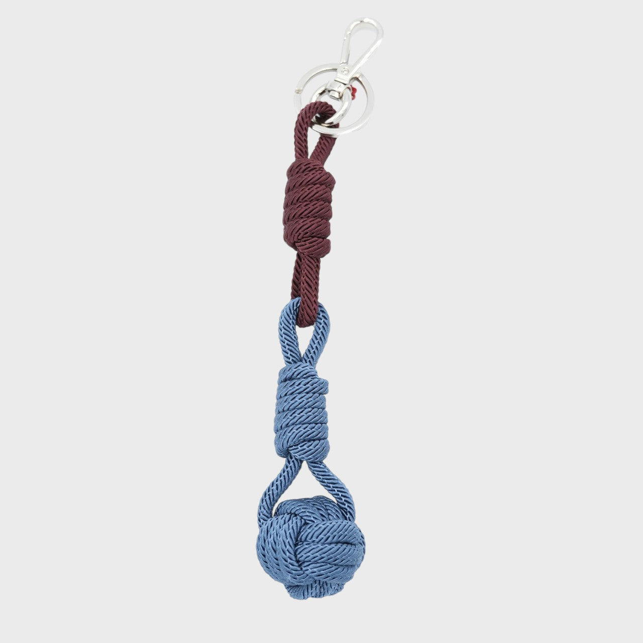 A macramé keychain representing a ball inspired by sailors knots. The straight upper part is burgundy and the ball part is blue. 