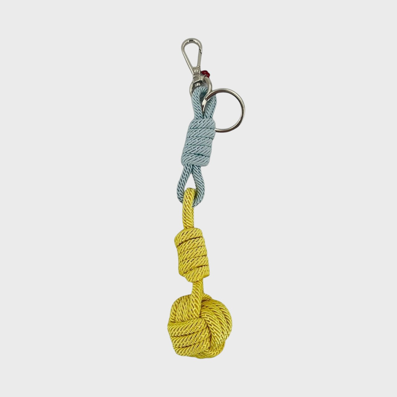 A macramé keychain representing a ball inspired by sailors knots. The straight upper part is light blue and the ball part is yellow. 