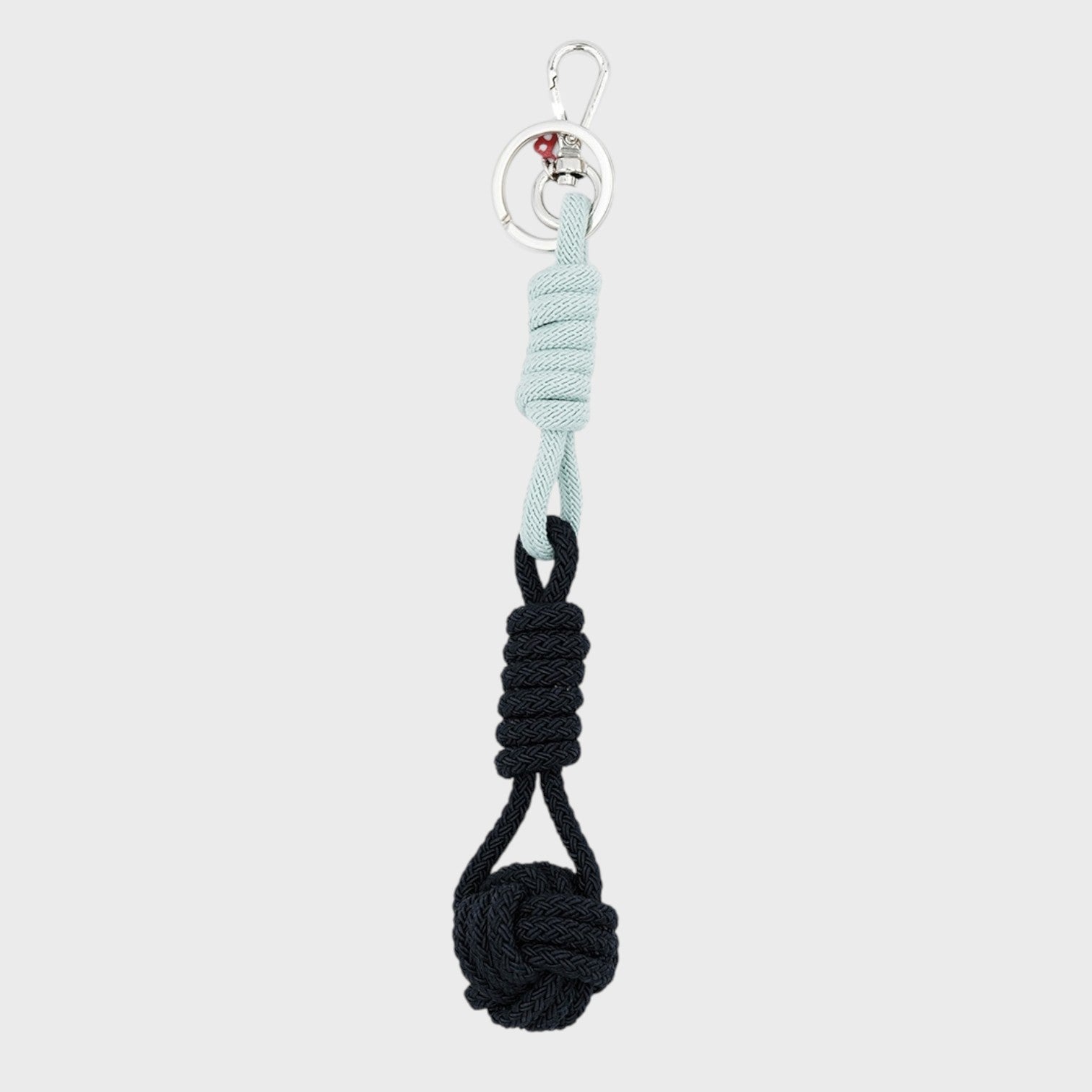 A macramé keychain representing a ball inspired by sailors knots. The straight upper part is light blue and the ball part is dark blue. 