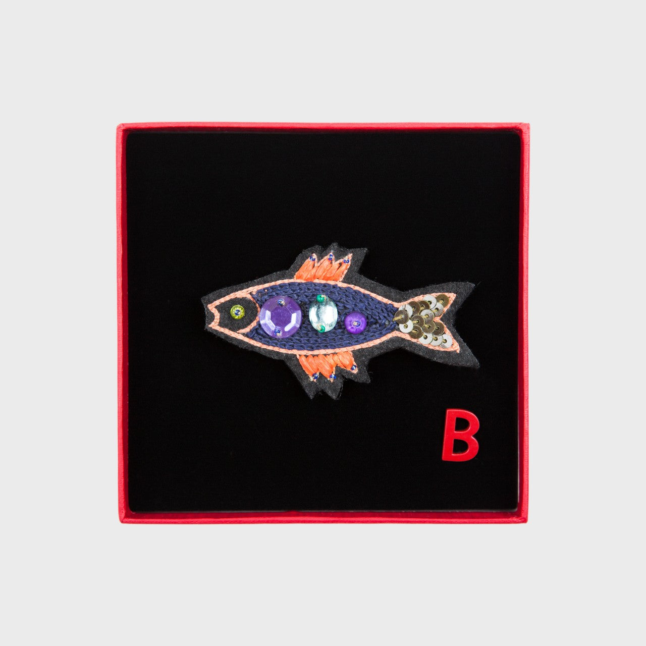An embroidered brooch representing a navy sardine in a box. 