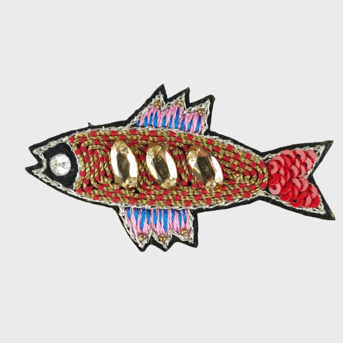 An embroidered brooch representing a red sardine with golden and pink details. 