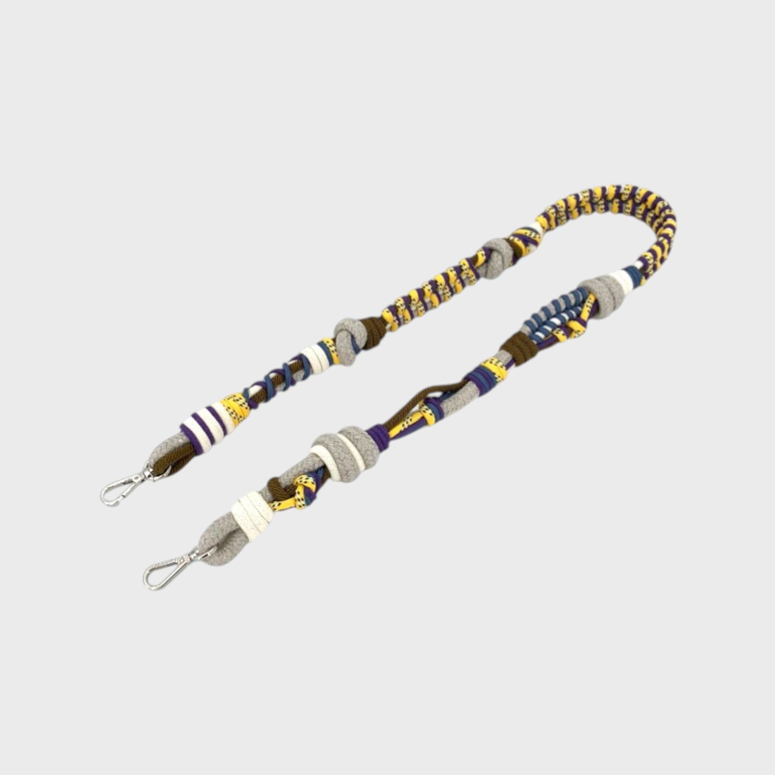 Multicolored braided macramé bag strap in bright yellow, dark green and purple, with white, shown on a light gray background.