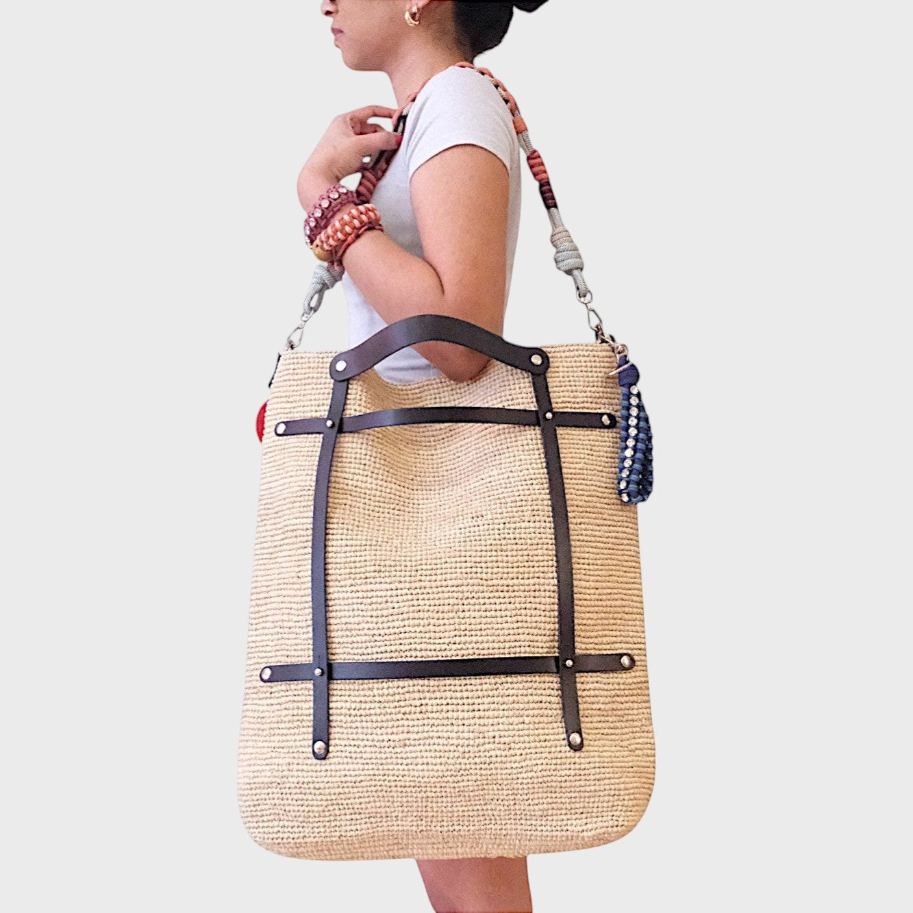 A model carrying on her shoulder the Optimiste tote bag with black leather and natural raffia. 