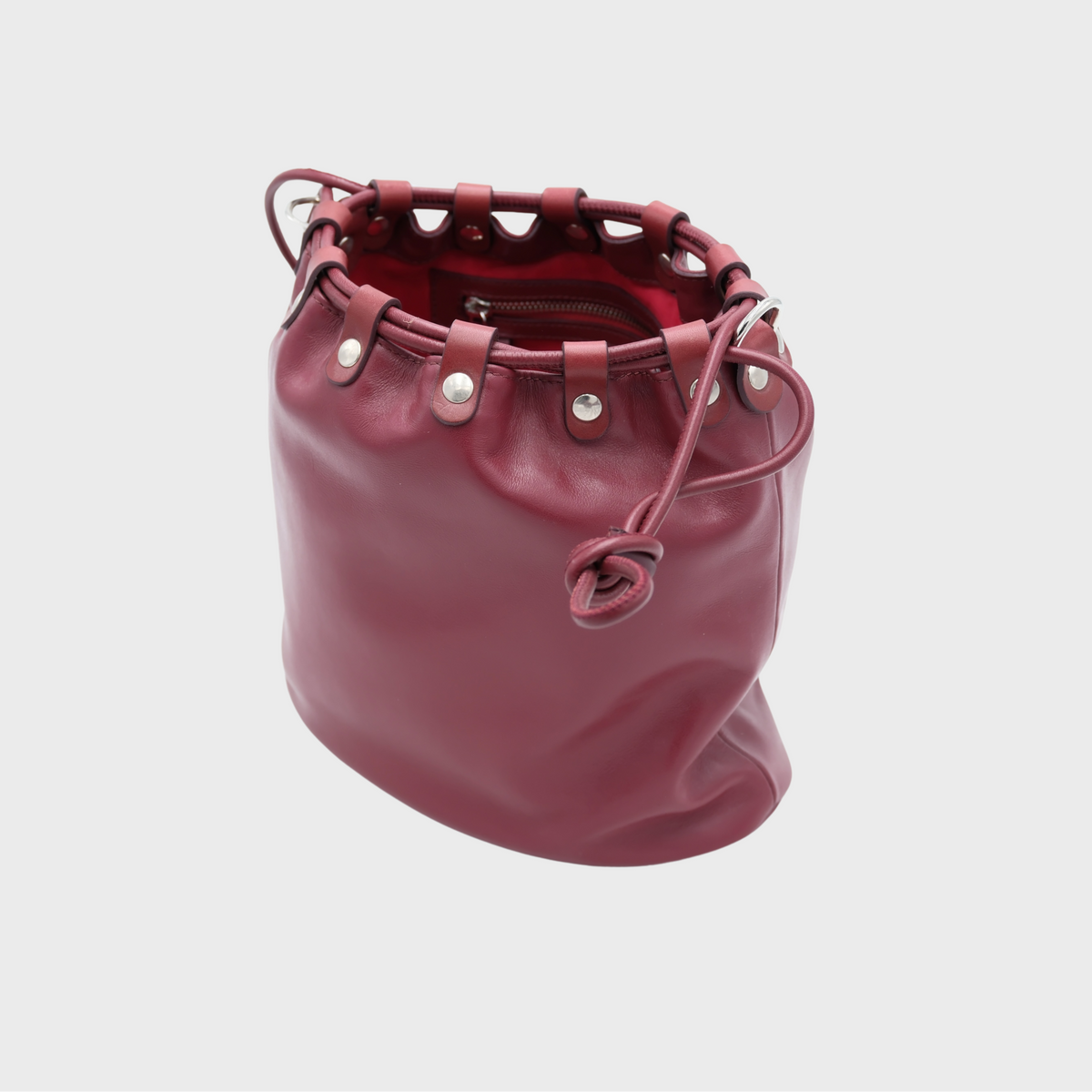 A burgundy leather bucket bag with a drawstring closure and silver-tone hardware, shown against a light gray background.