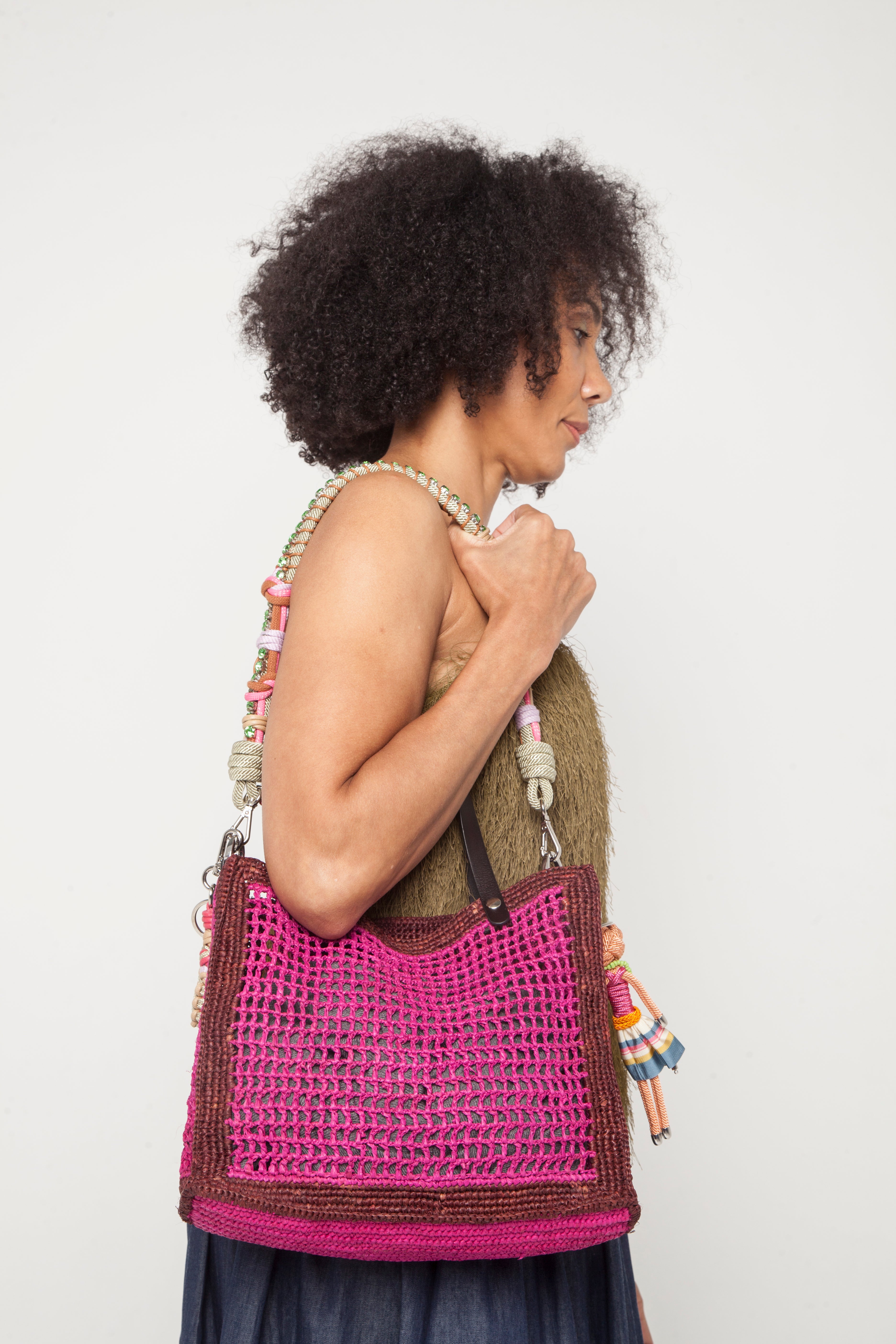 A model carrying on her shoulder the pink cabas handbag with the green and pink strap. 