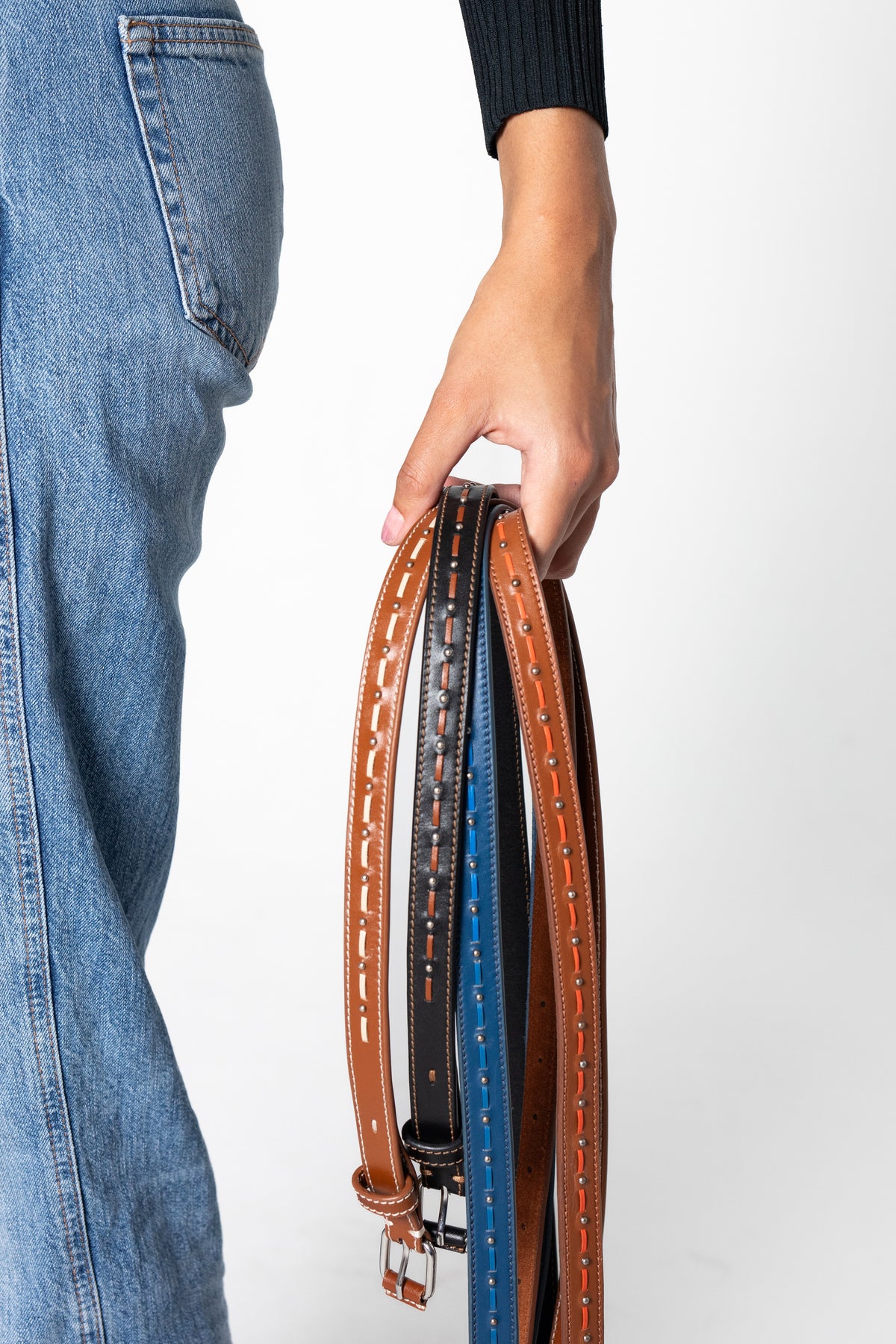 Person holding four leather belts of different colors on a white background