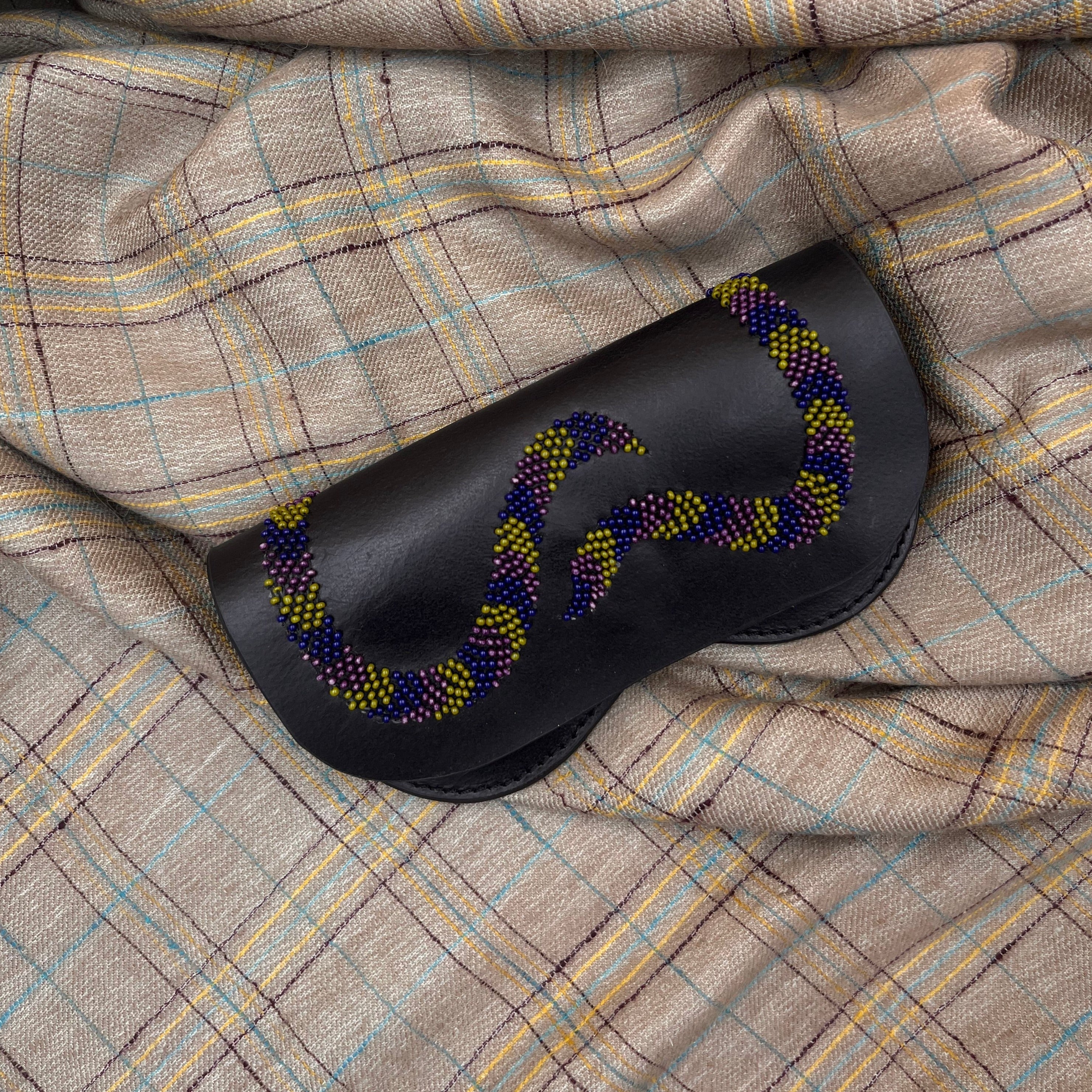 A dark blue leather snake glasses case on a grey blanket. 