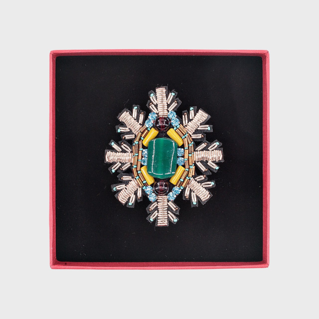 An embroidered brooch representing a snowflake with a green stoned center in a box. 