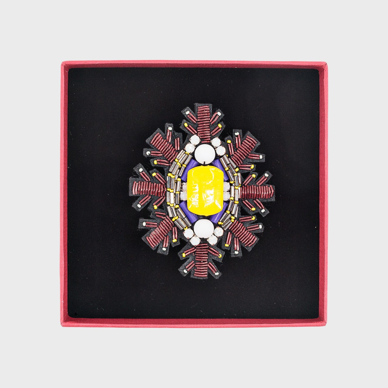 An embroidered brooch representing a snowflake with a yellow stoned center in a box. 