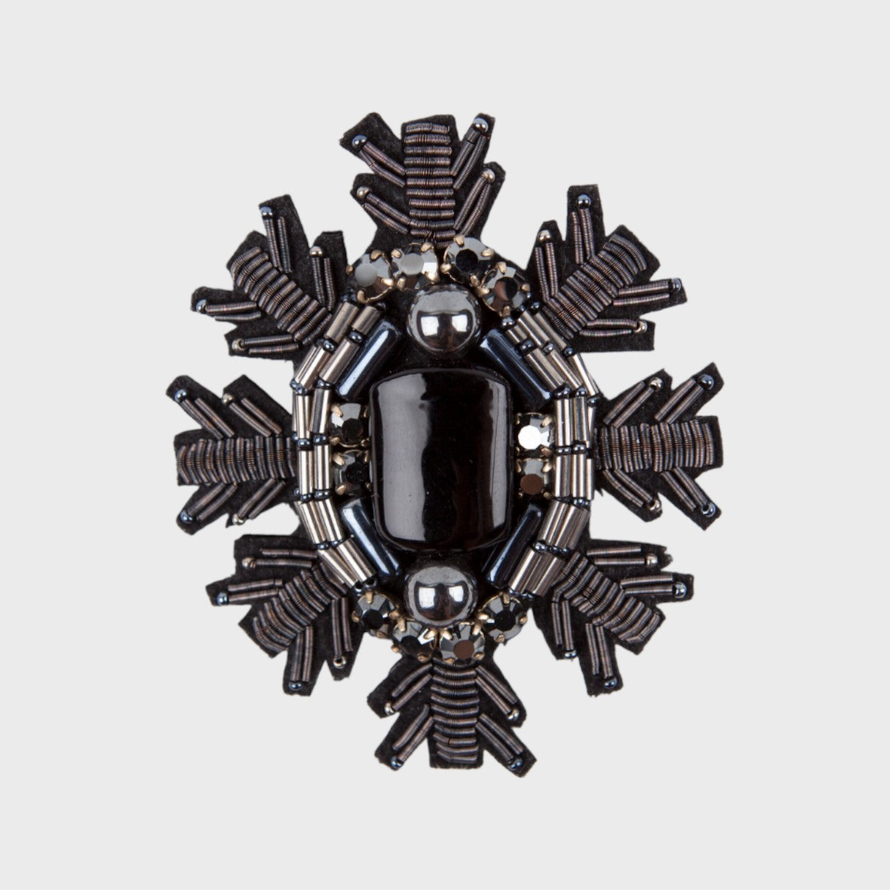 An embroidered brooch representing a black snowflake with a black stone at the center of it. 