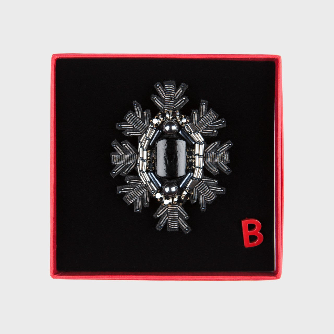 A black embroidered brooch representing a snowflake in a box. 