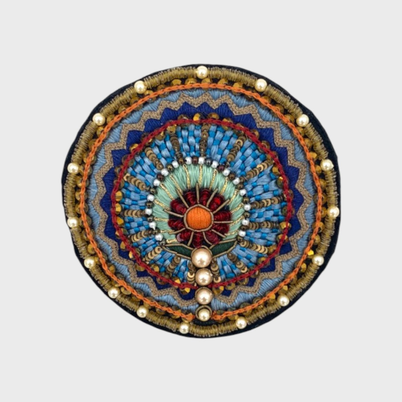 An embroidered brooch with yellow, blue, beige and red details. 