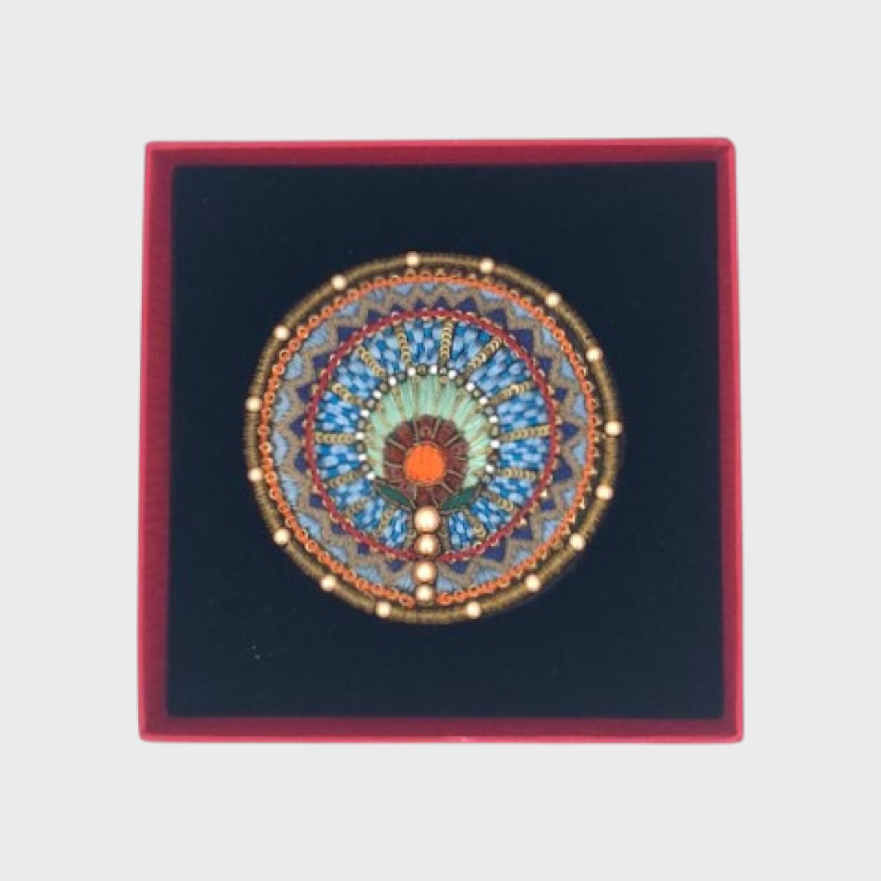 An embroidered brooch with multicolor details in a box. 