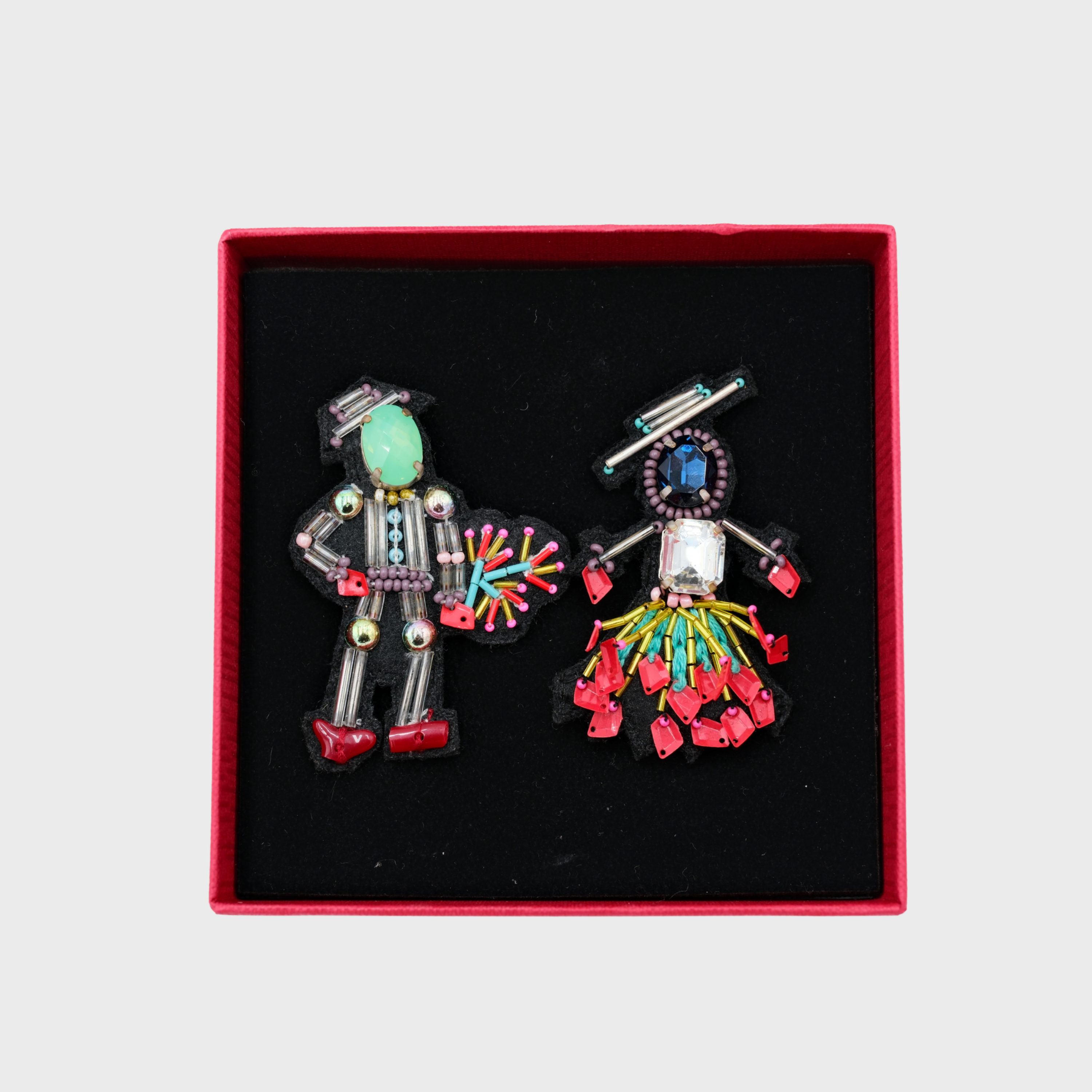 An embroidered set of two brooches representing a couple with blue heads in a box. 