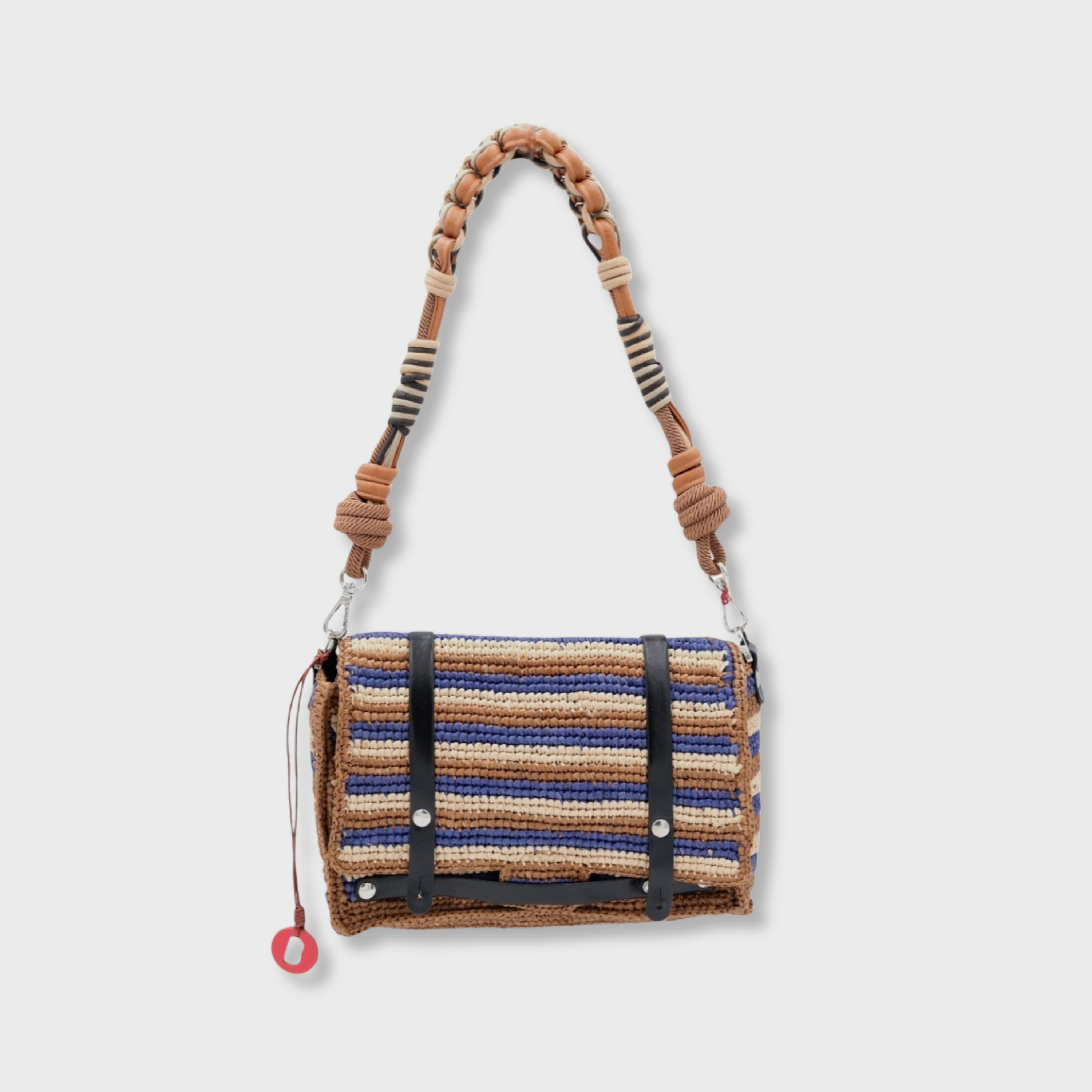 A brown, beige and blue striped raffia shoulder bag with black leather straps hanging by a colorful macramé braided strap featuring brown leather and brown macramé, set against a light gray background.