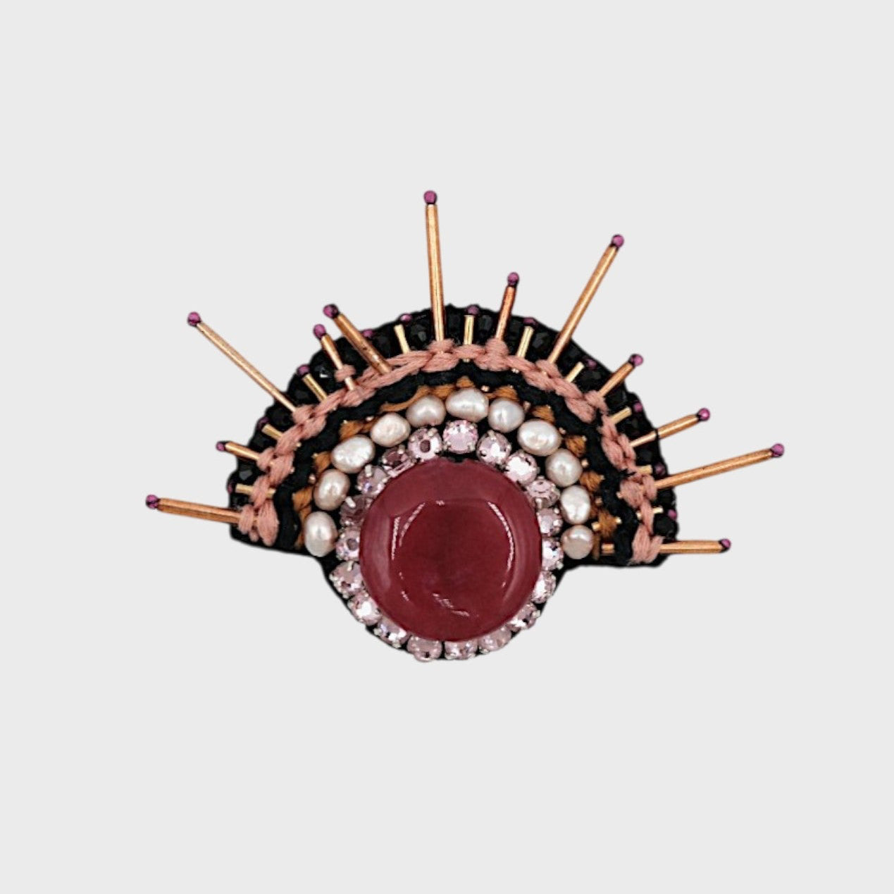 An embroidered brooch representing a sunrise woth white and pink details and a red centered stone. 