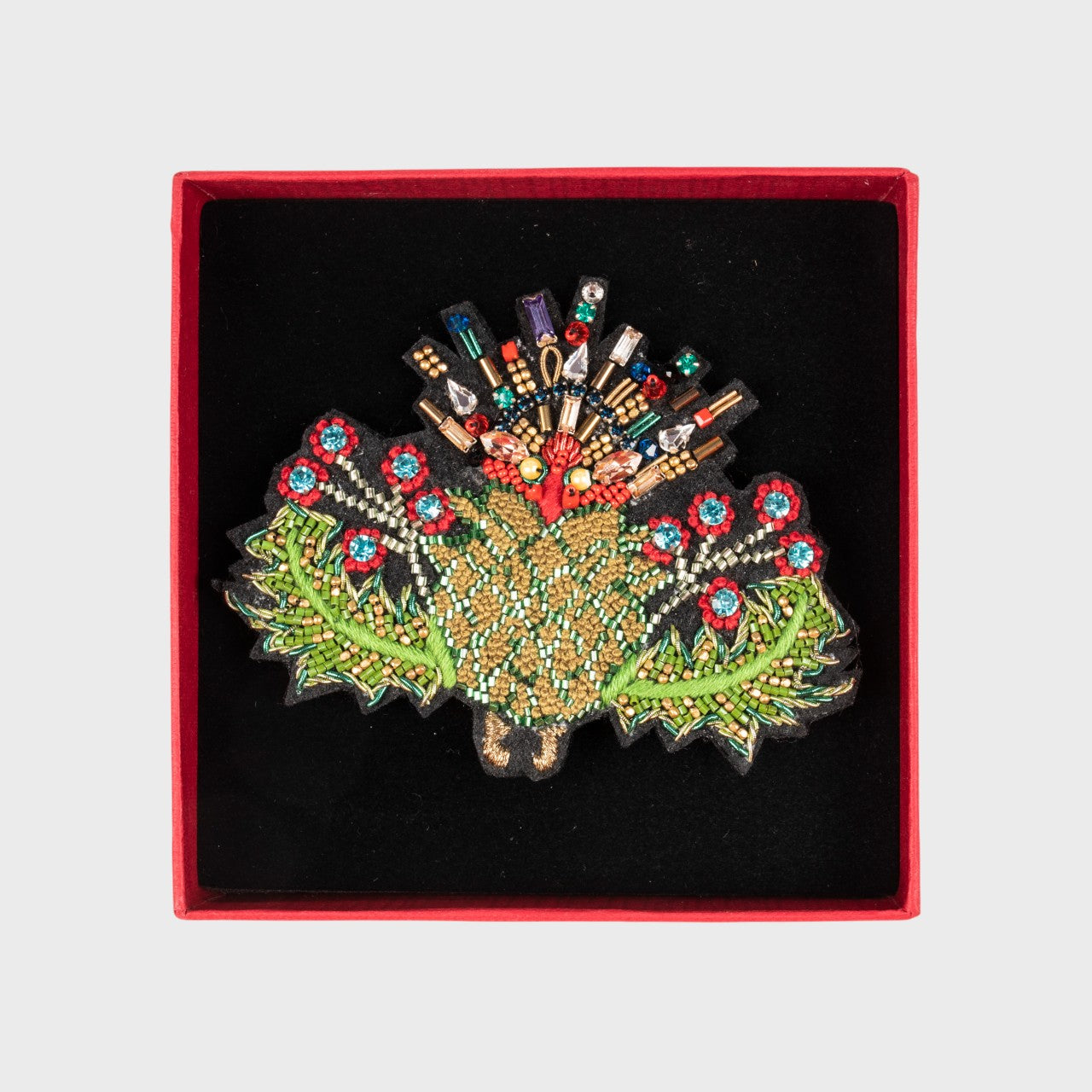 An embroidered brooch representing a thistle flower in a box. 