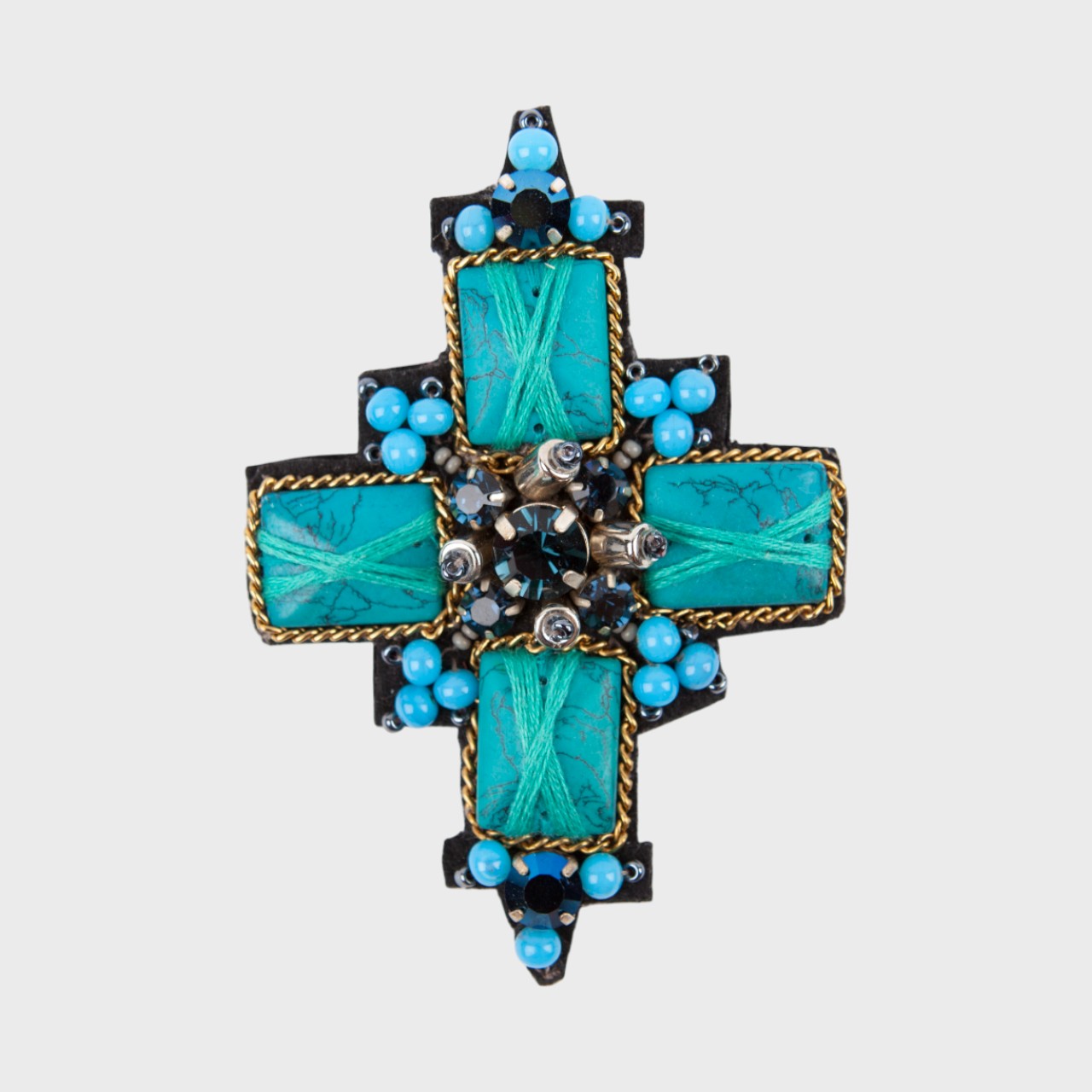 An embroidered brooch representing a blue cross with four blue stones and blue details around. 