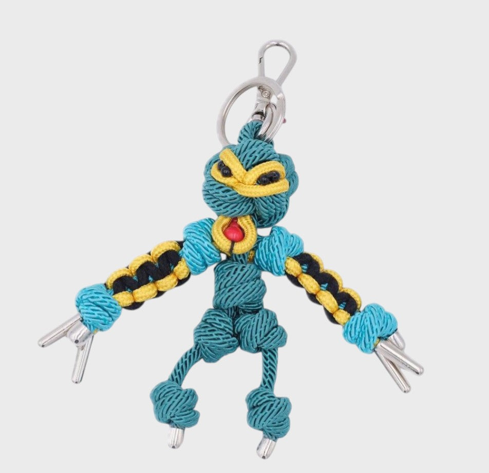 Handmade blue and yellow macramé bag charm featuring a character, meant to represent a Polynesian divinity. They are attached to a silver clasp.