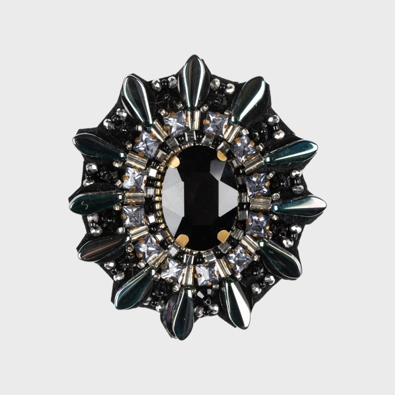 An embroidered brooch representing a turtle with a black stoned middle and black details around. 