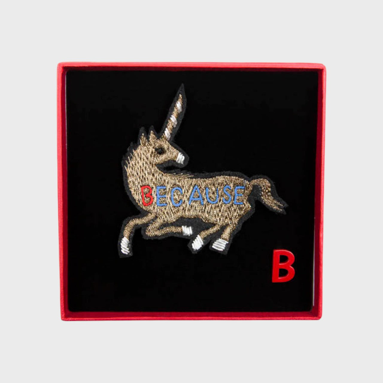 An embroidered brooch representing a golden unicorn in a box. 