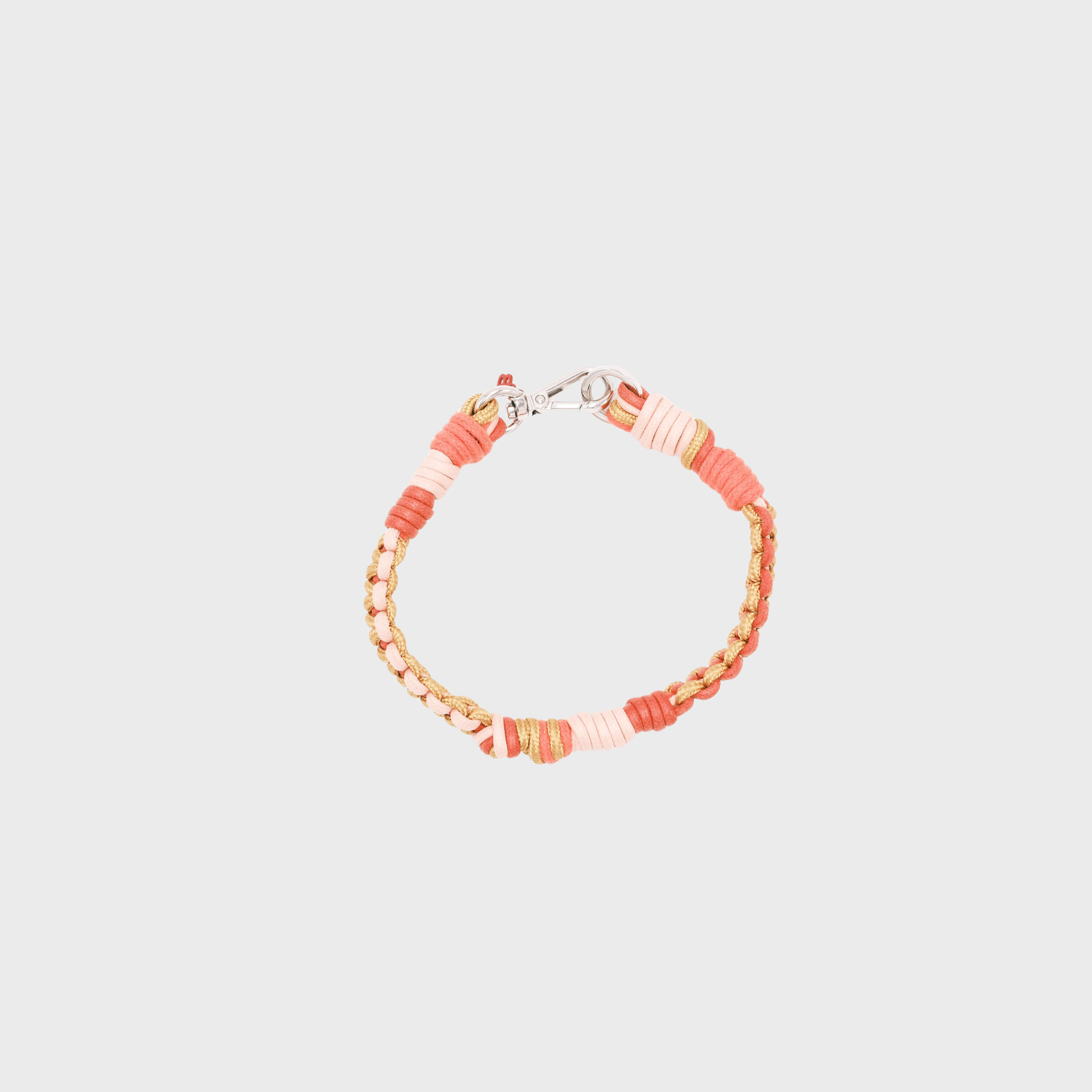 A photo taken from above of a braided macramé cord collar in shades of pink, peach, and beige with a silver clasp.