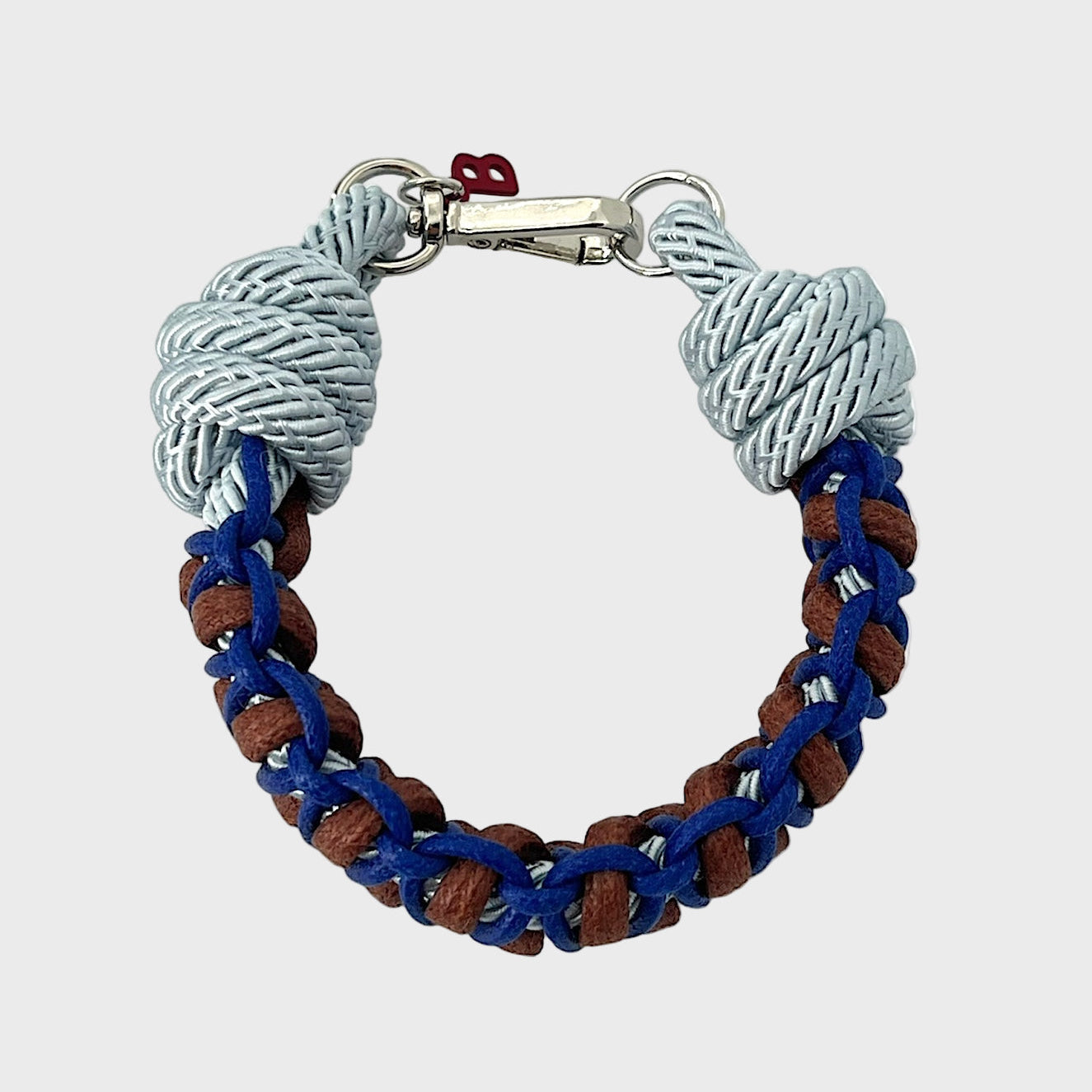 A photo taken from above of a braided macramé bracelet in shades of light and dark blue and brown with a silver clasp.