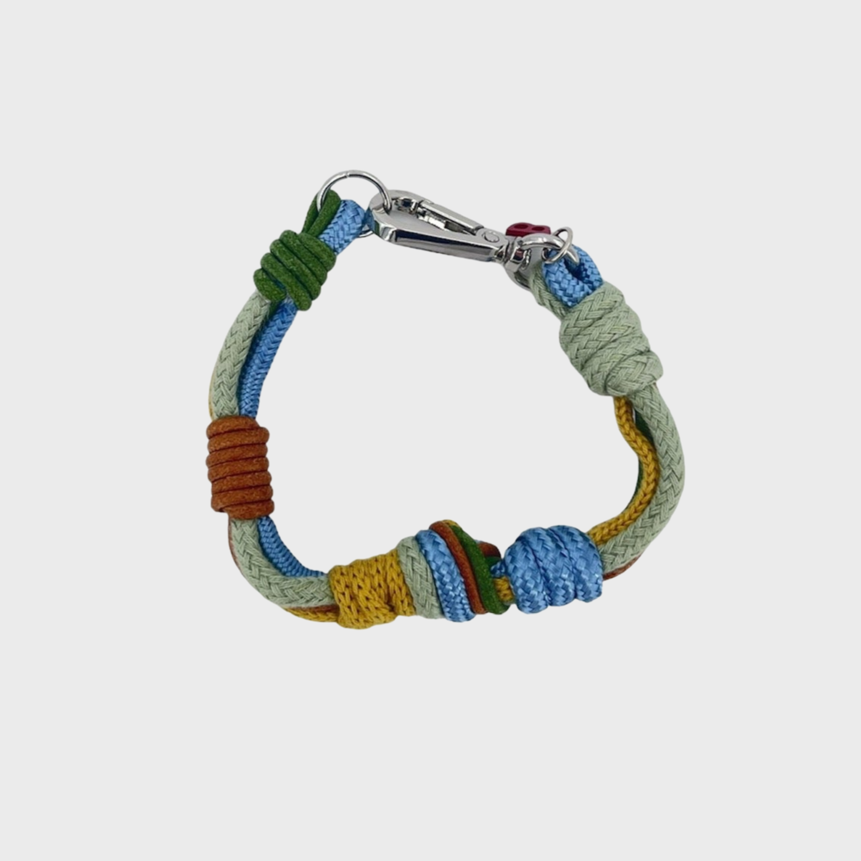 A macramé bracelet with knotted details, featuring shades of blue, green, brown and yellow, finished with a silver-tone metal clasp, set on a light gray background.
