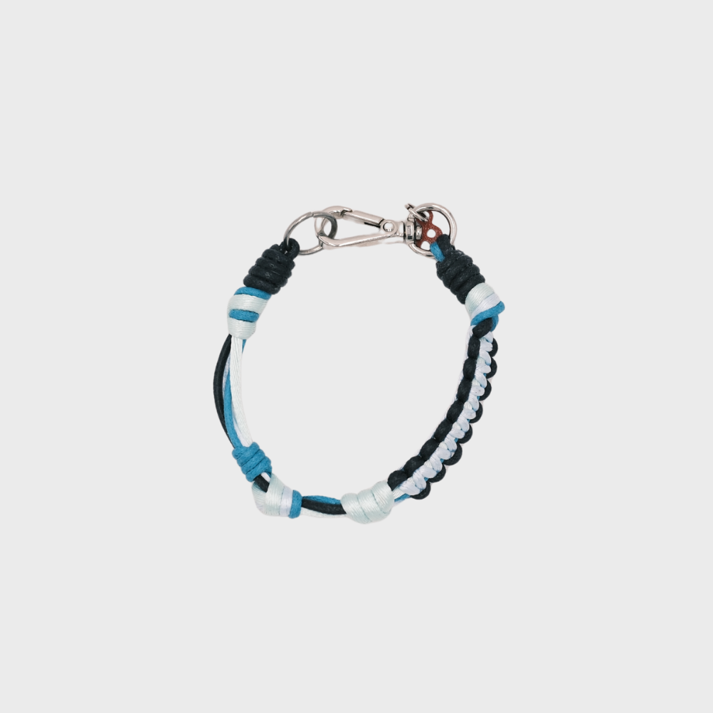 A photo taken from above of a thin braided macramé bracelet in shades of dark and light blue, with a silver clasp.