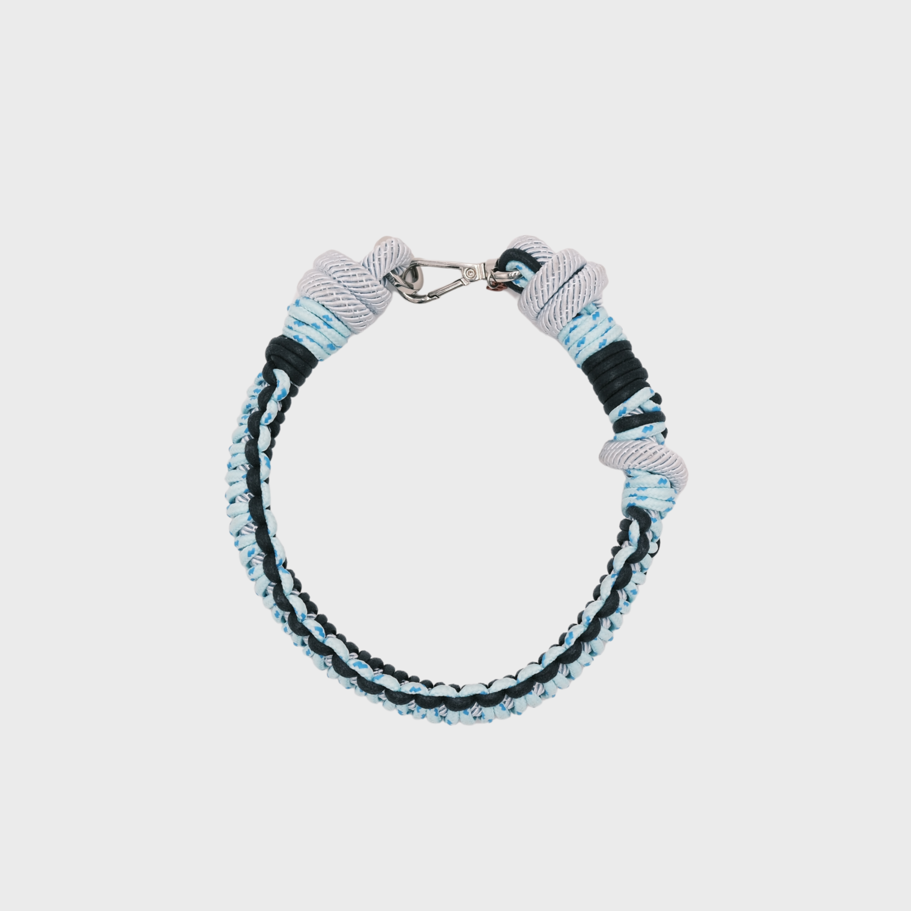 A photo taken from above of a braided macramé cord collar in shades of dark blue and light blue with a silver clasp.
