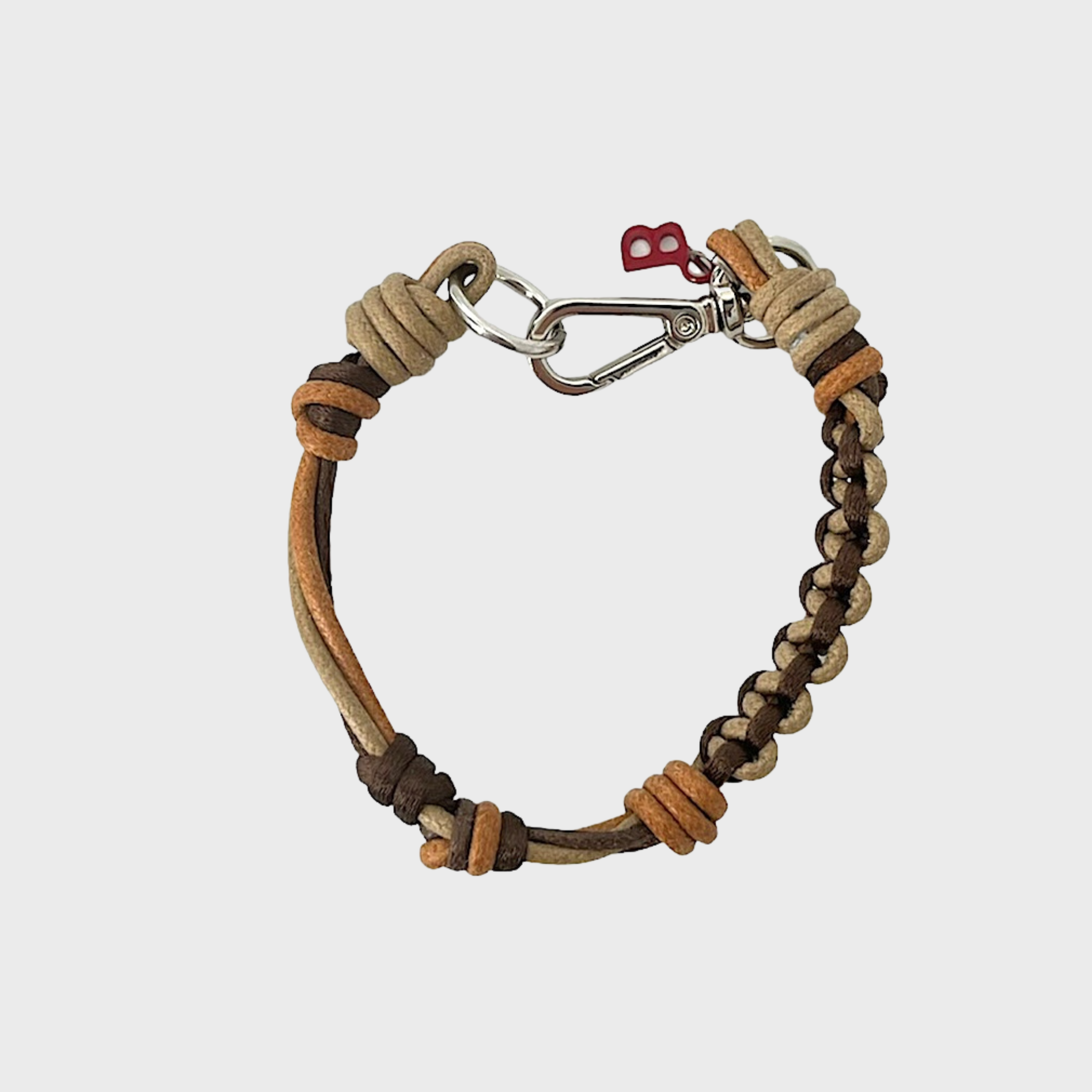 A photo taken from above of a thin braided macramé bracelet in shades of brown and beige, with a silver clasp.