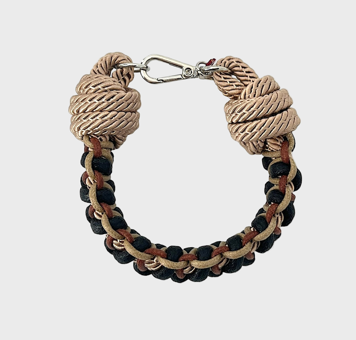 A photo taken from above of a braided macramé bracelet in shades of beige, black and brown with a silver clasp.