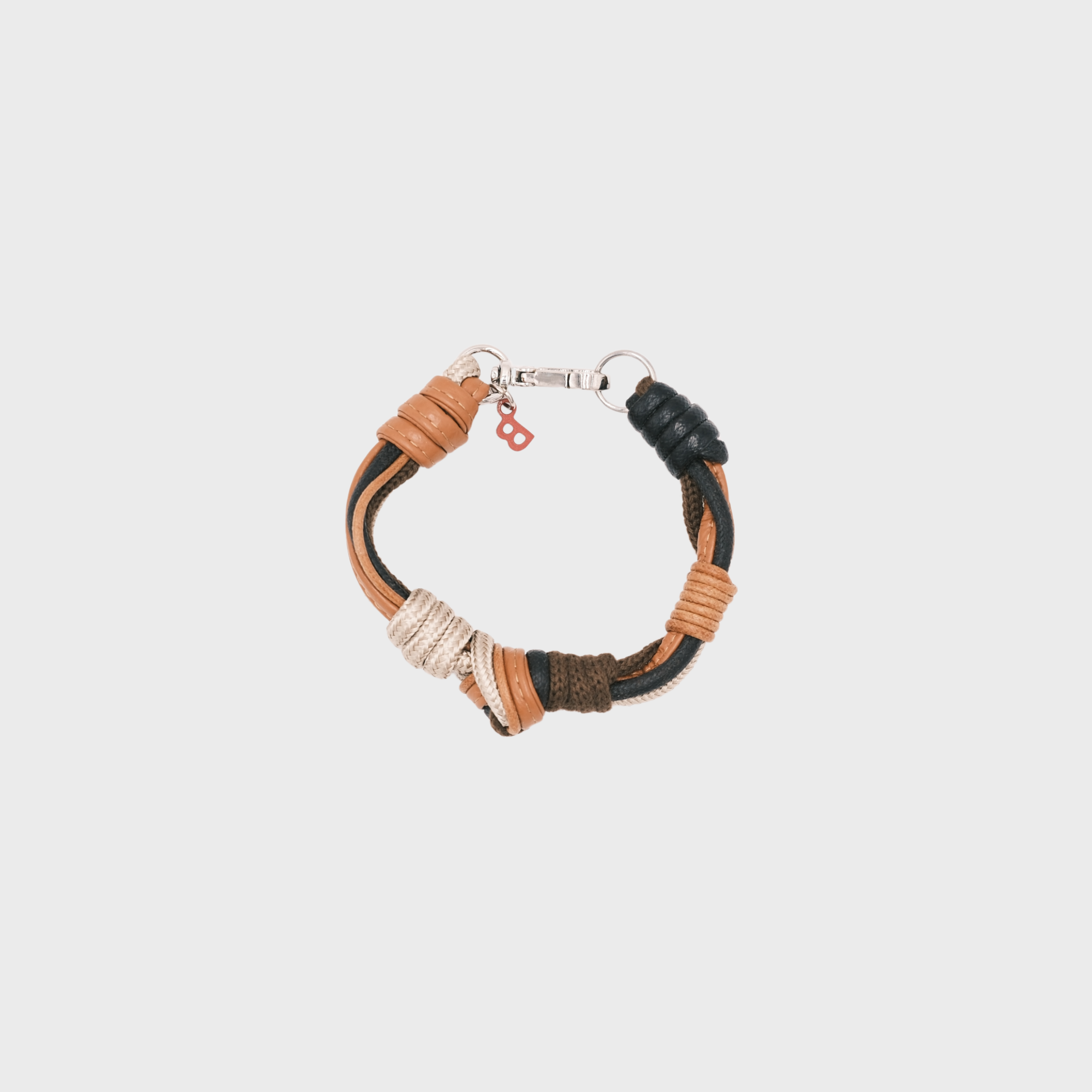 A photo taken from above of a knotted leather and macramé bracelet in shades of brown, black and beige, with a silver clasp.