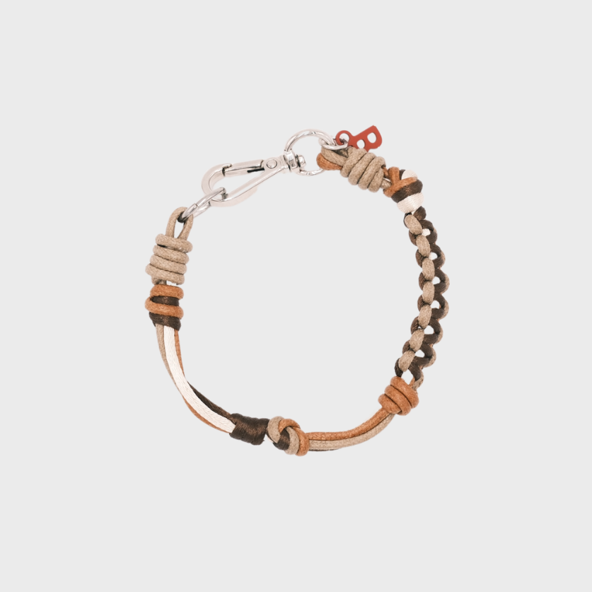 A photo taken from above of a thin braided macramé bracelet in shades of brown, with a silver clasp.
