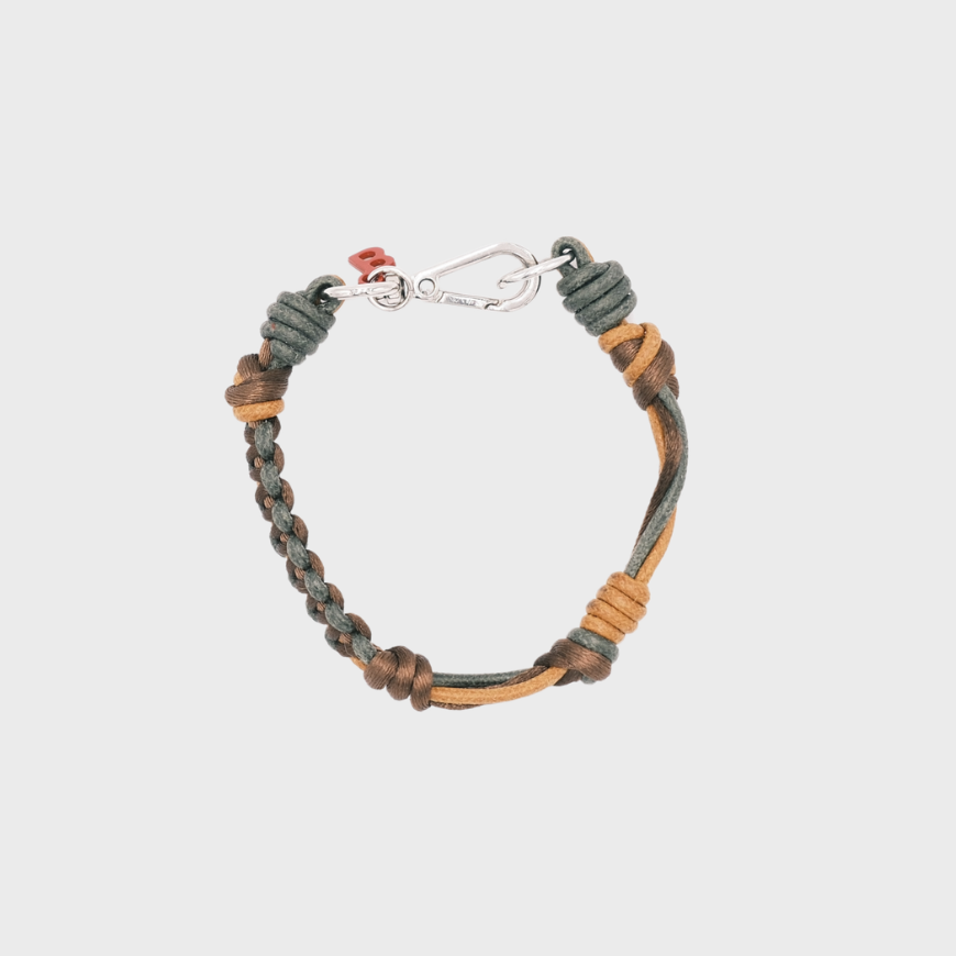 A photo taken from above of a thin braided macramé bracelet in shades of green and mustard, with a silver clasp.