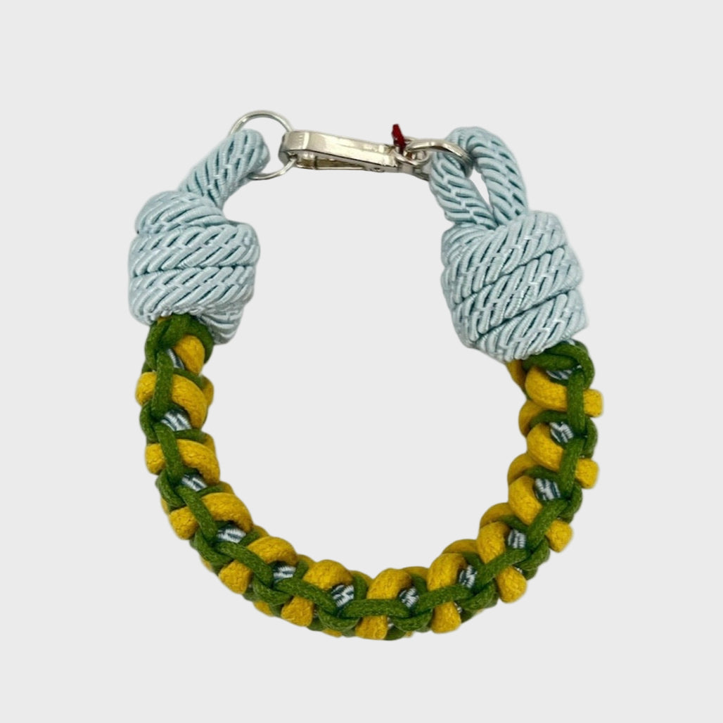 A photo taken from above of a braided macramé bracelet in shades of green, yellow and light blue with a silver clasp.