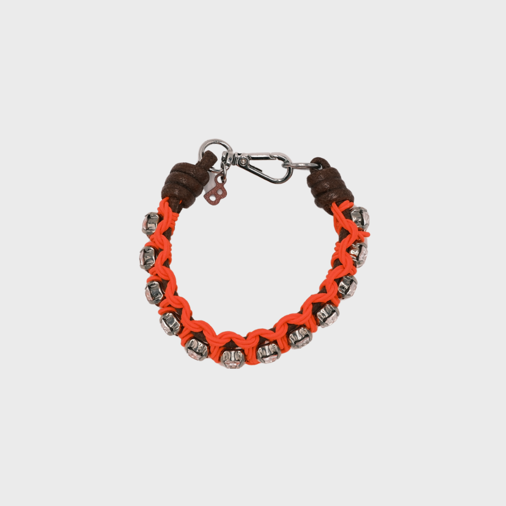 A handmade macramé woven bracelet featuring a mix of brown, and neon orange threads, accented with small white beads and a silver clasp.