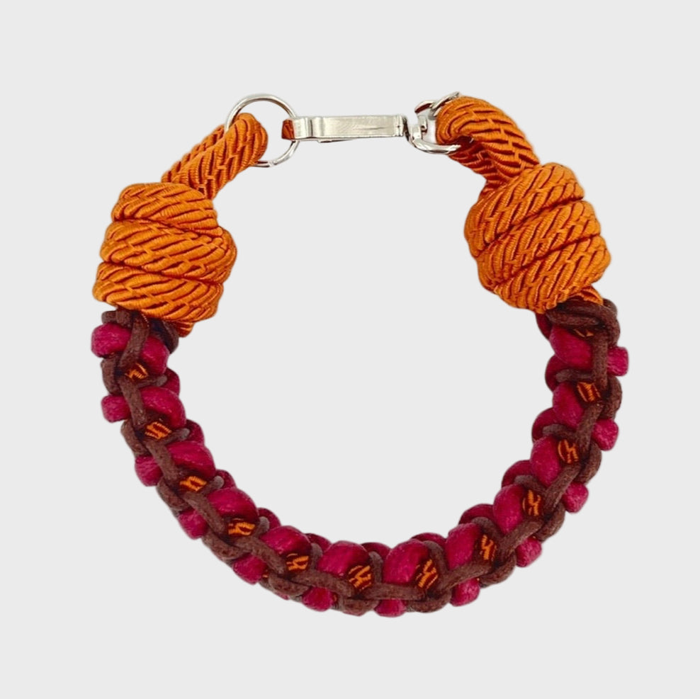 A photo taken from above of a braided macramé bracelet in shades of fuchsia, brown and orange with a silver clasp.