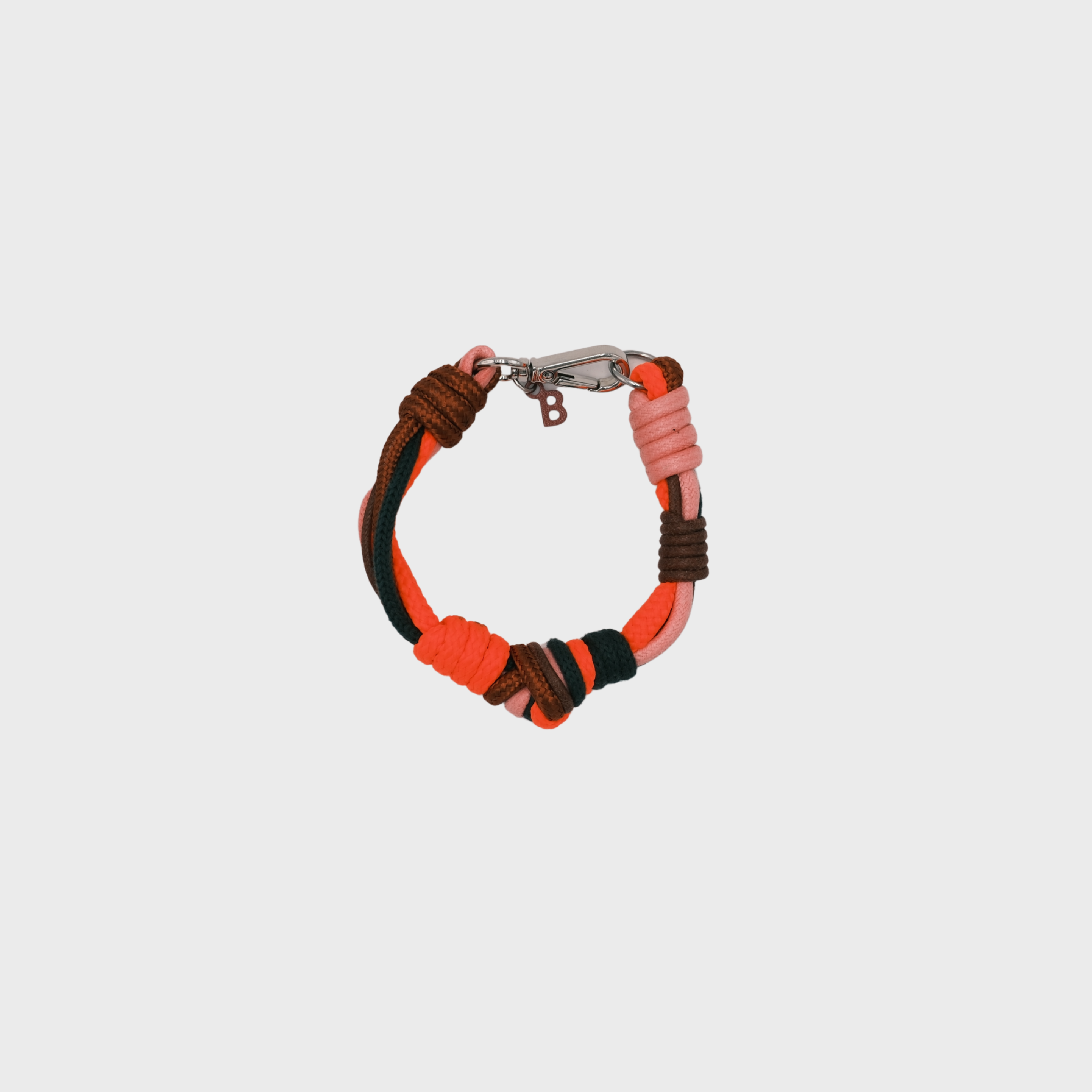 A photo taken from above of a knotted macramé bracelet in shades of neon orange, brown and green, with a silver clasp.