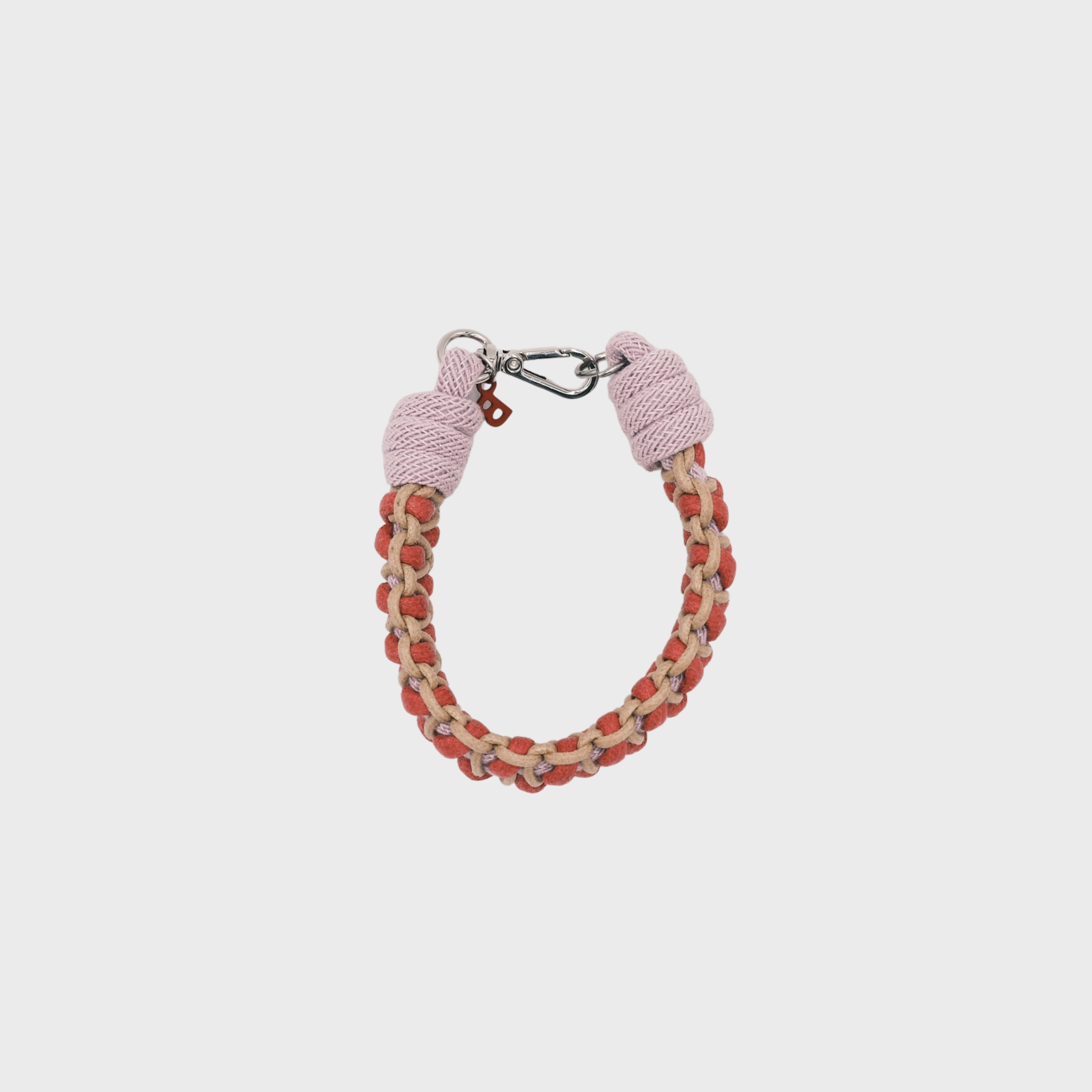 A photo taken from above of a braided macramé bracelet in shades of bright pink, light pink, and beige with a silver clasp.