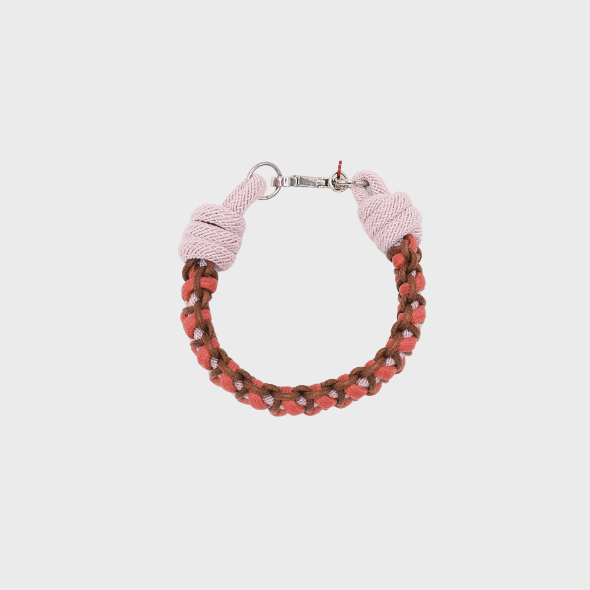 A photo taken from above of a braided macramé bracelet in shades of bright pink, light pink, and brown with a silver clasp.