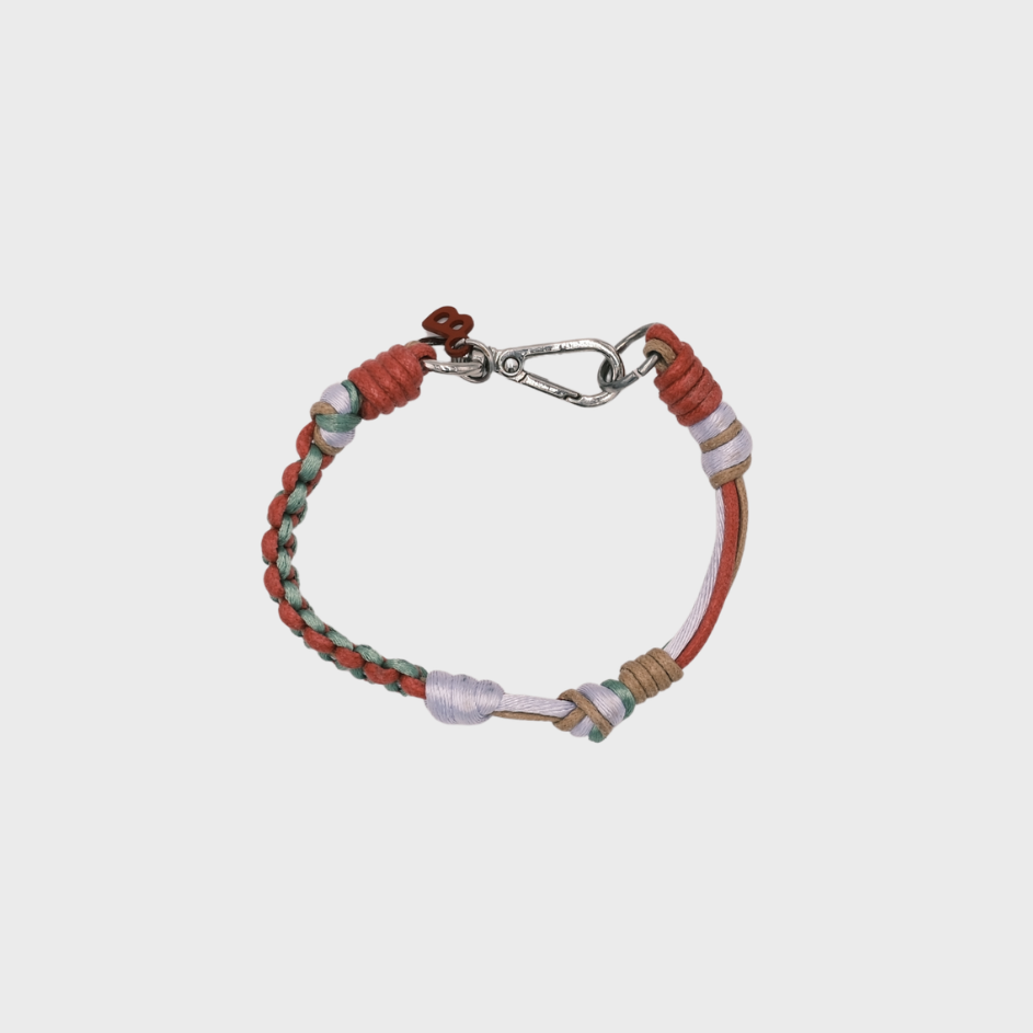 A photo taken from above of a thin braided macramé bracelet in shades of pink, green and light brown, with a silver clasp.