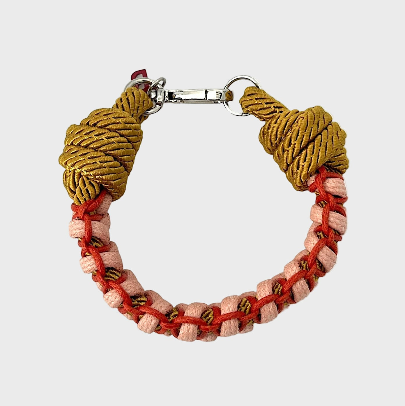 A photo taken from above of a braided macramé bracelet in shades of red, light pink and yellow with a silver clasp.