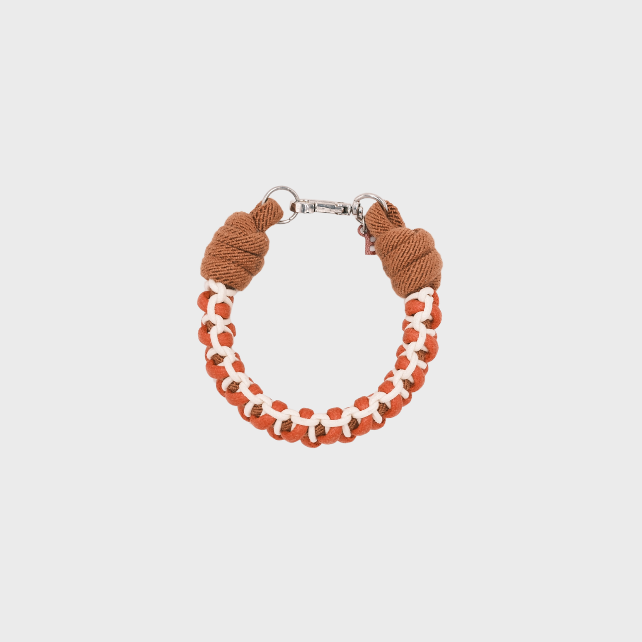 A photo taken from above of a braided macramé bracelet in shades of red, white and brown with a silver clasp.